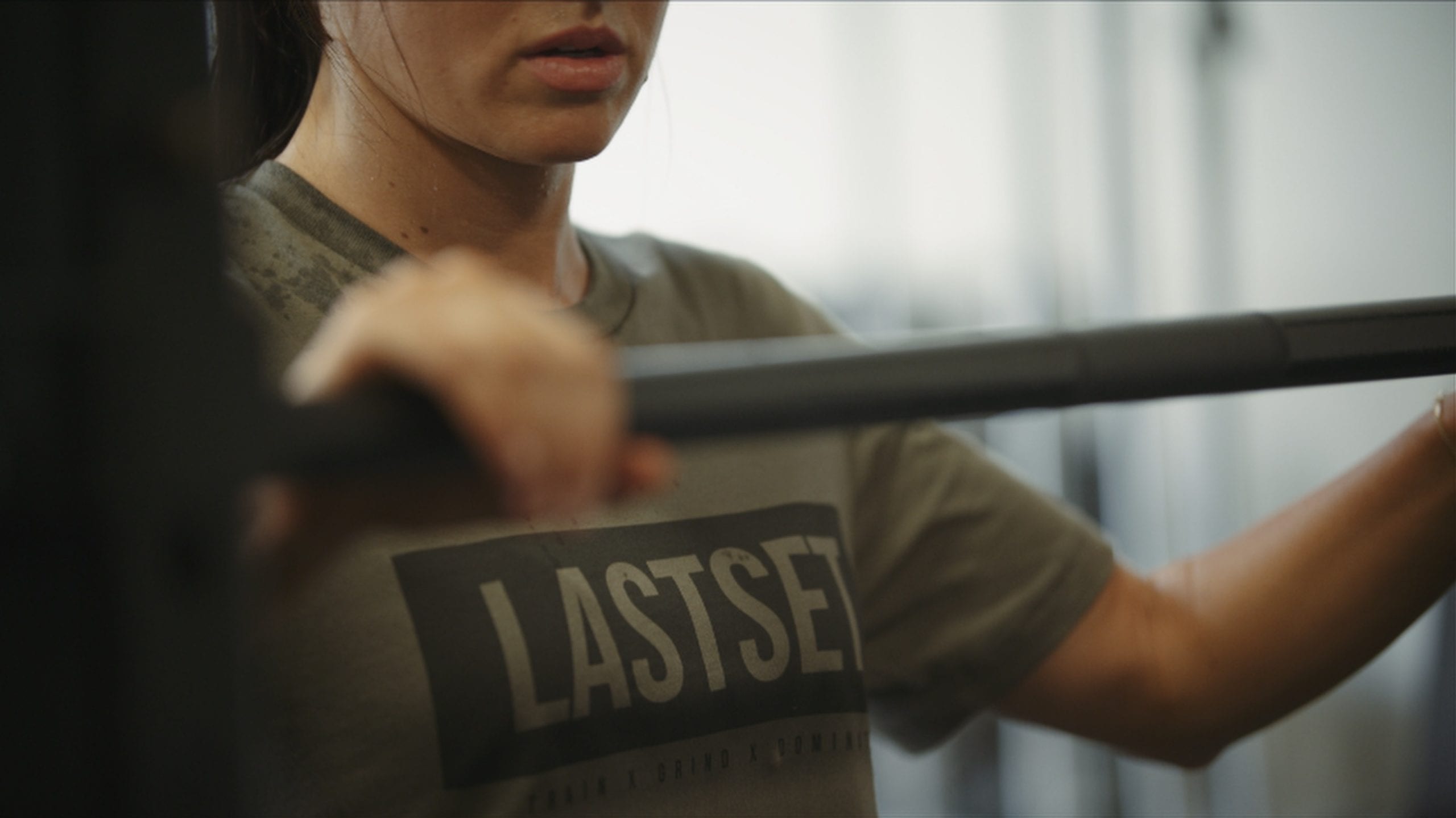 Closeup of woman in a gray t shirt holding weight bar