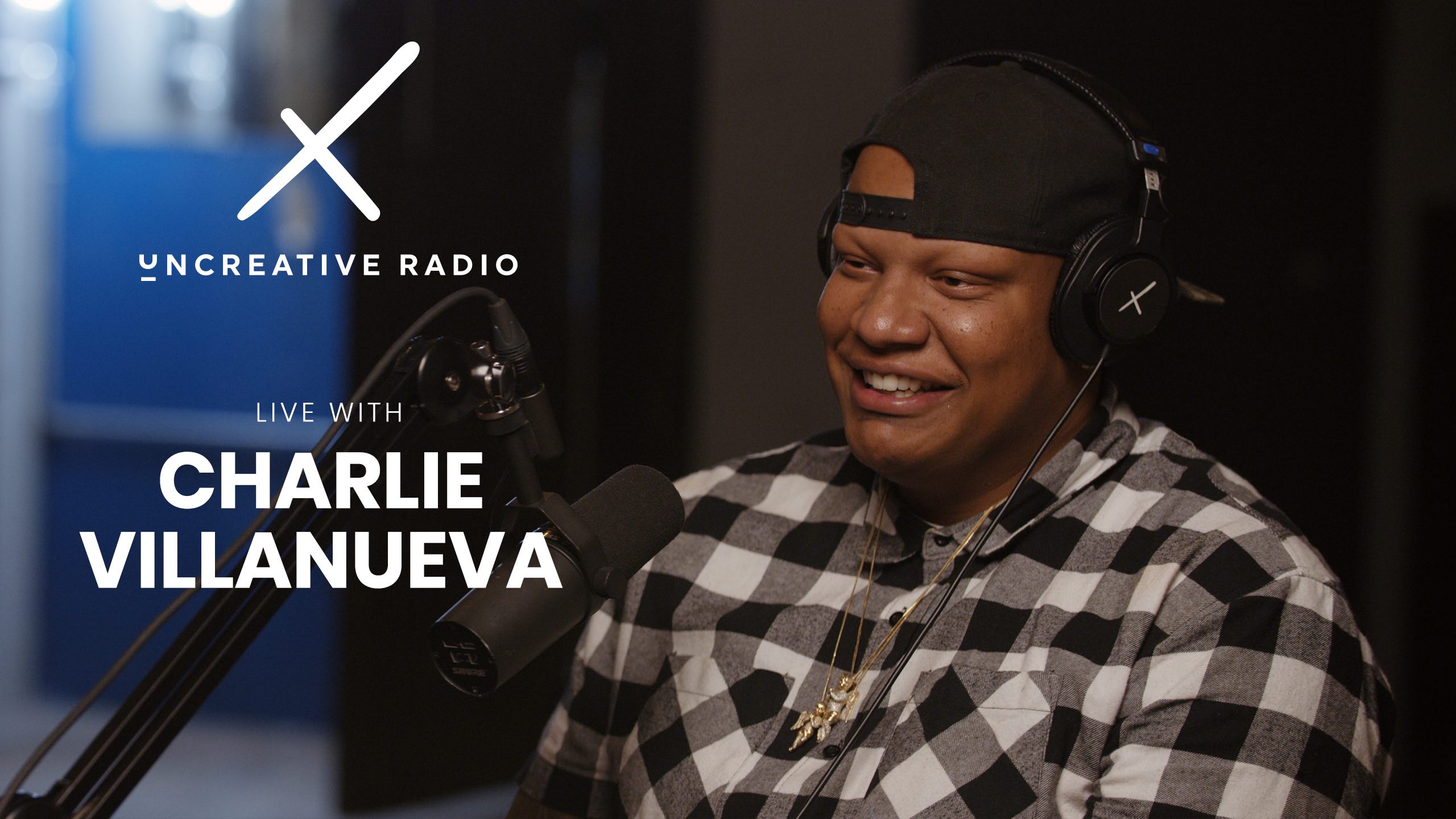 IU C&I Studios Page White Uncreative Radio Live With Charlie Villanueva logo with him wearing a black cap backwards and a black and white checkered shirt by a microphone and smiling
