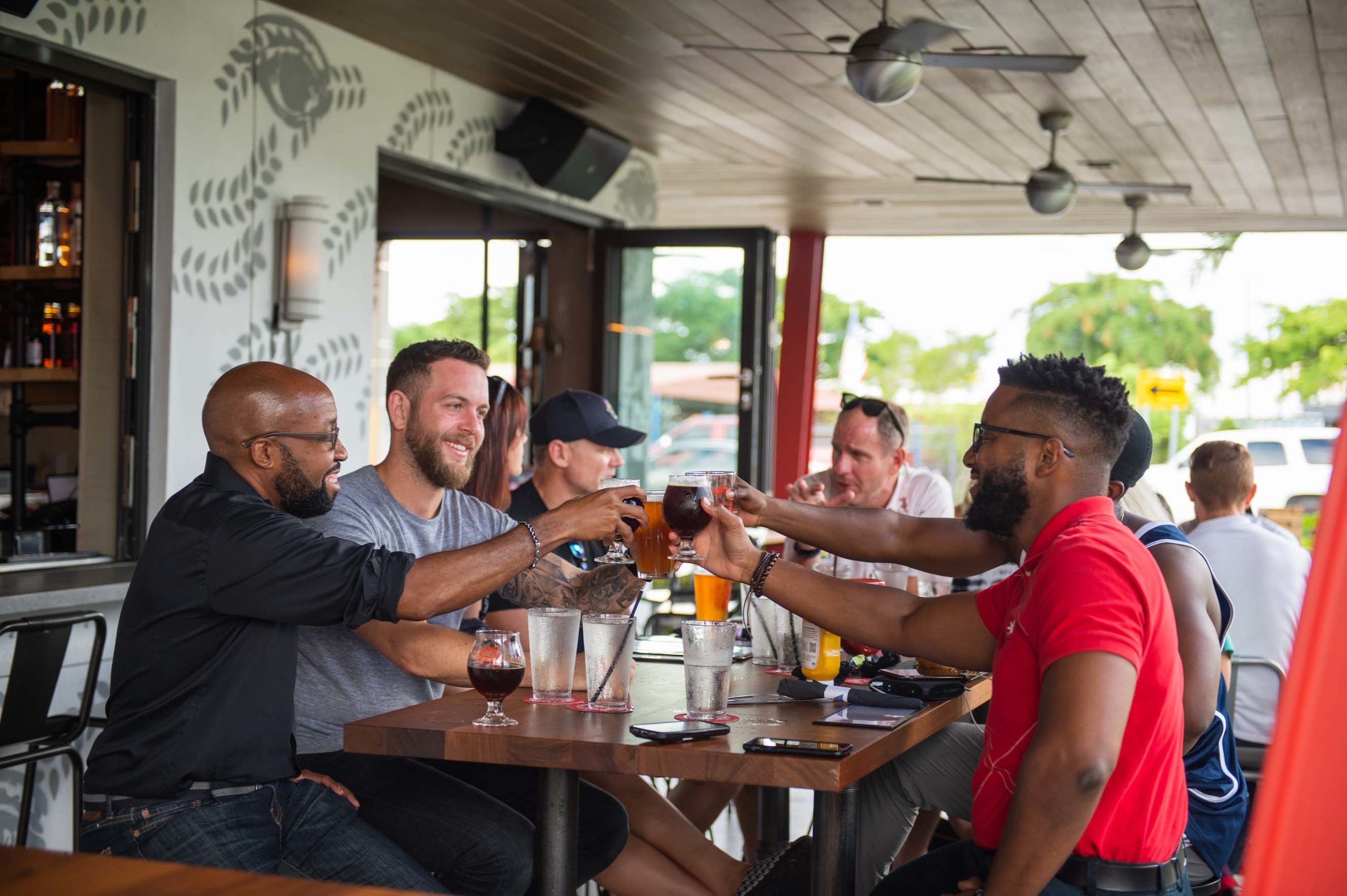Freebird Real Estate Experts East Fort Lauderdale Group of men sitting at a wooden table with some toasting drinks and smiling in a restaurant