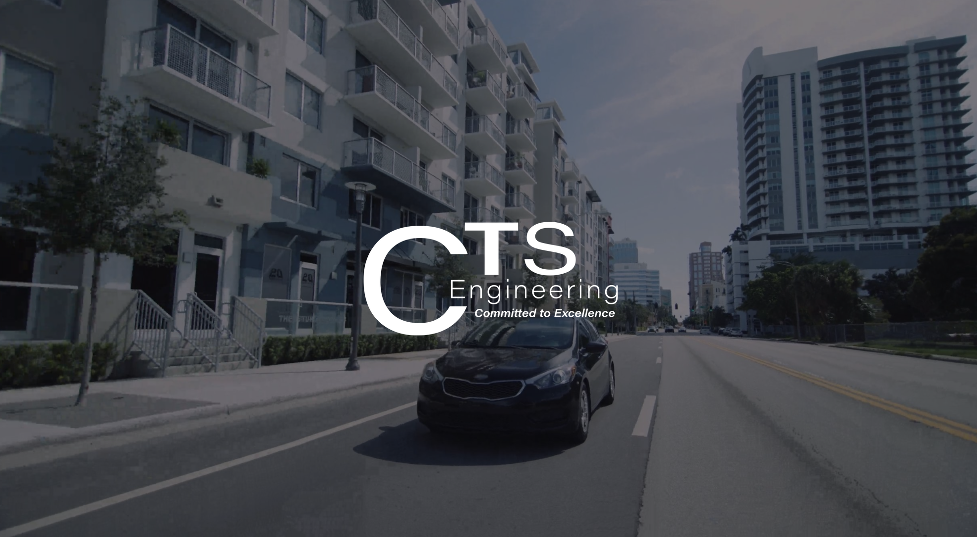 IU C&I Studios Page White CTS Engineering Committed to Excellence logo with dimmed background view from front of a black car driving down a road in a city