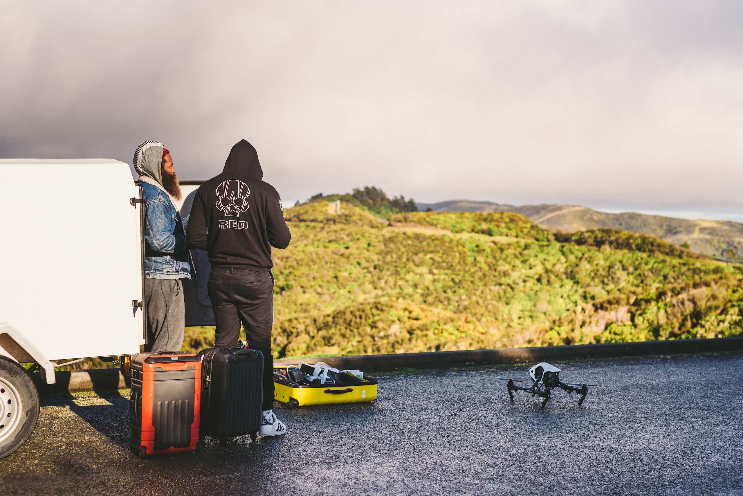 Two crew members by a white fan looking out over a valley with drone and equipment around them