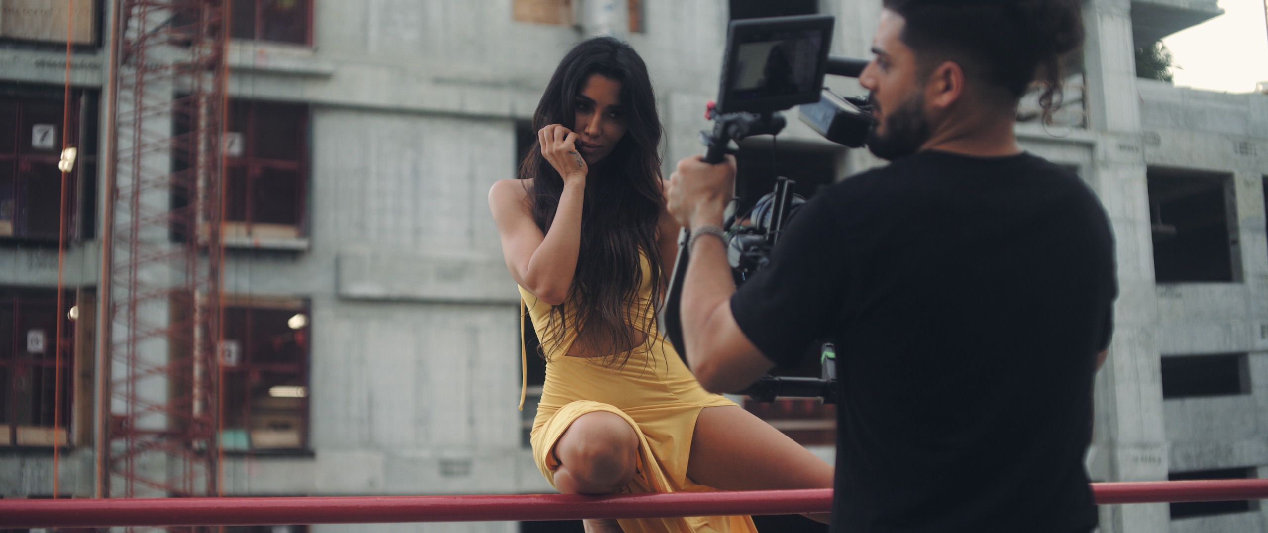 Video Production Company Fort Lauderdale Metisha posing in a yellow dress sitting on red railing of building with male crew member filming her