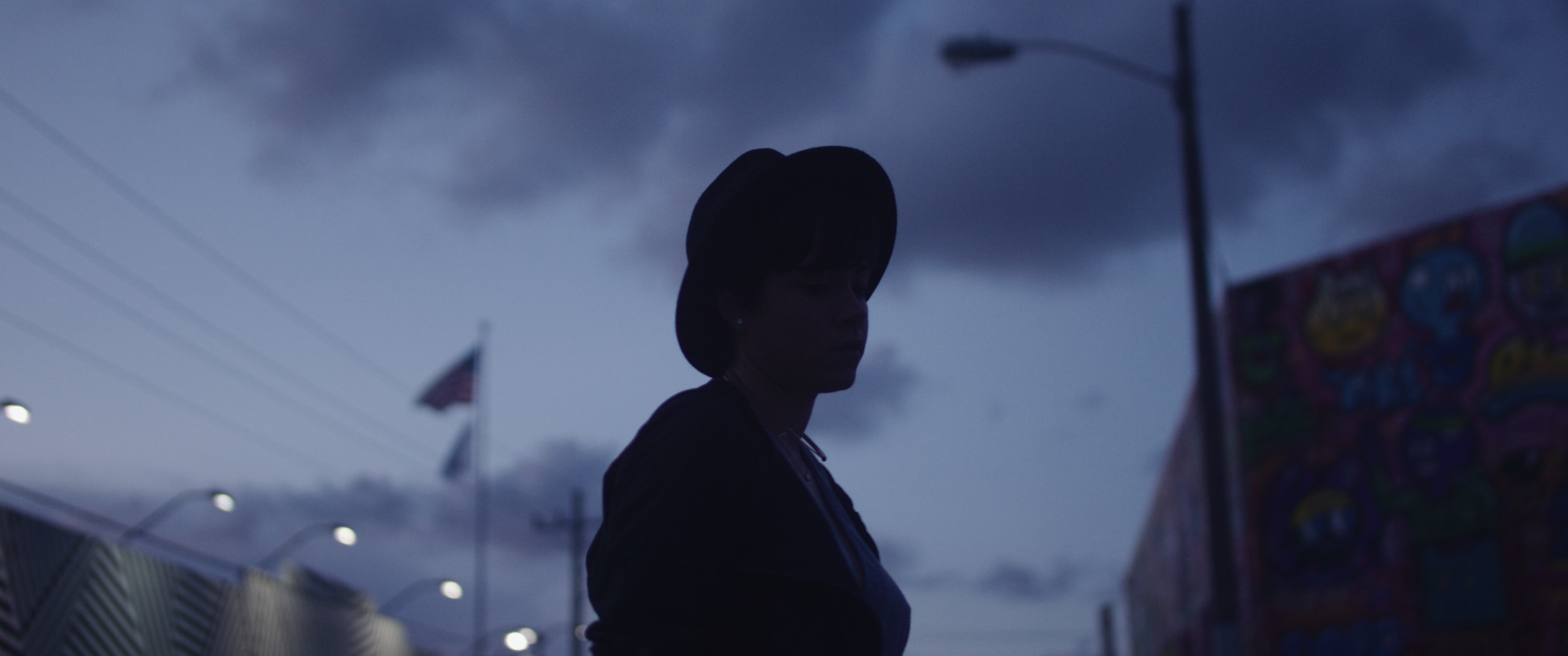 From Miami I Love You Side profile silhouette of woman wearing a hat looking down on a street in semi darkness