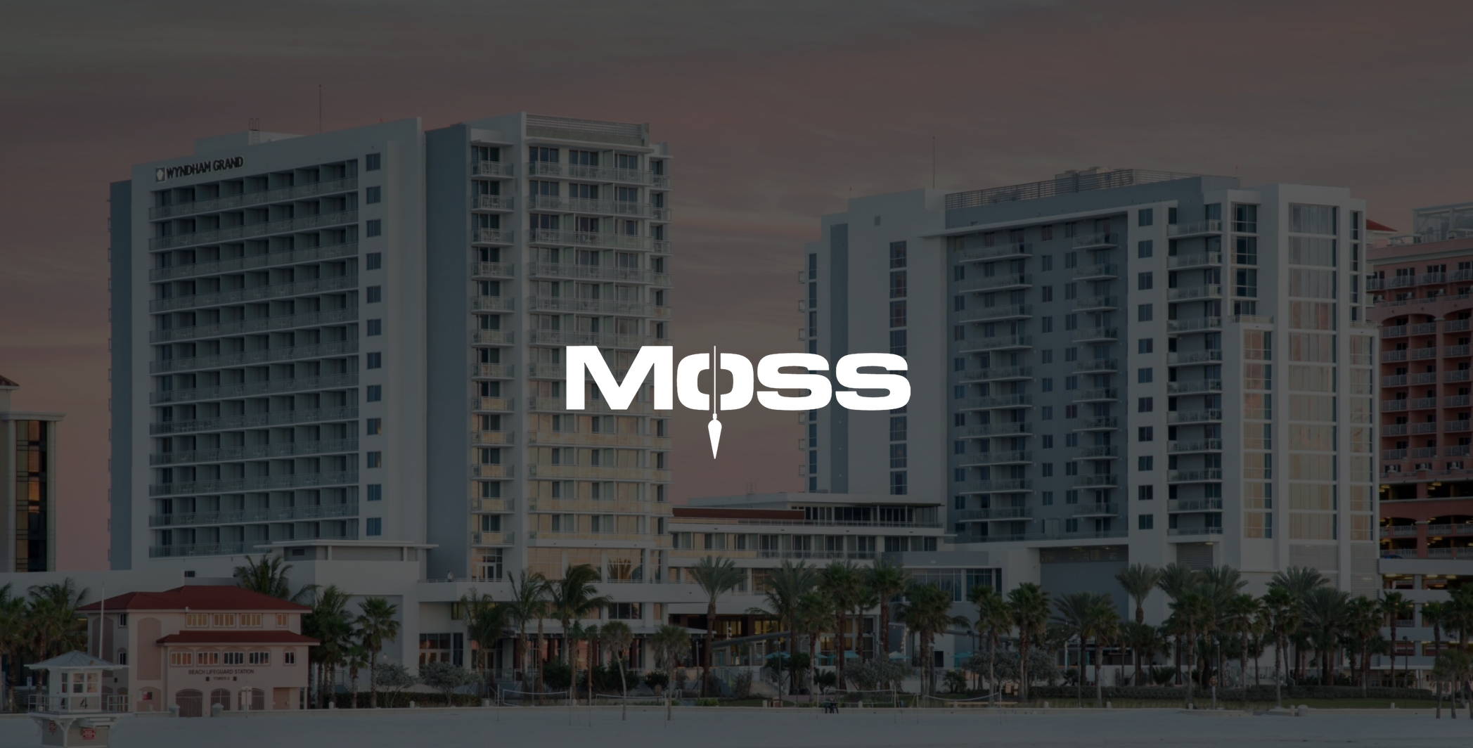IU C&I Studios Page White Moss logo Construction Fort Lauderdale with dimmed background of two Wyndham Grand buildings by a beach