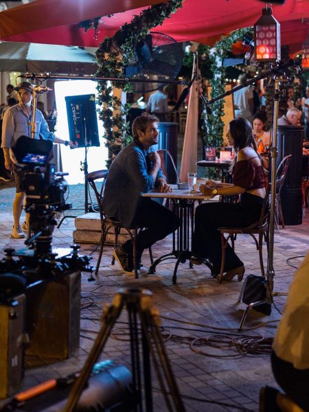 Love and War Feature film mastering and delivery services by C&I Studios Crew members with equipment in front of man and woman sitting at a table in a restaurant
