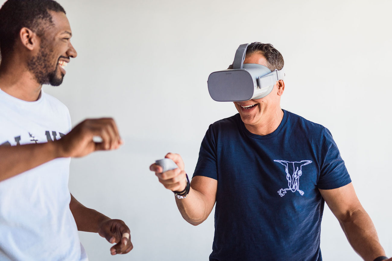 Joshua Miller with smiling man wearing blue shirt using a controller using virtual reality glasses