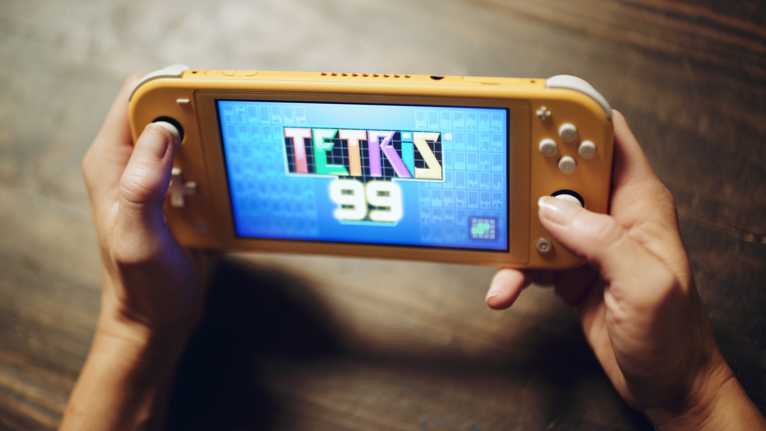 Closeup of hands holding a video game console with Tetris 99 game title screen loading