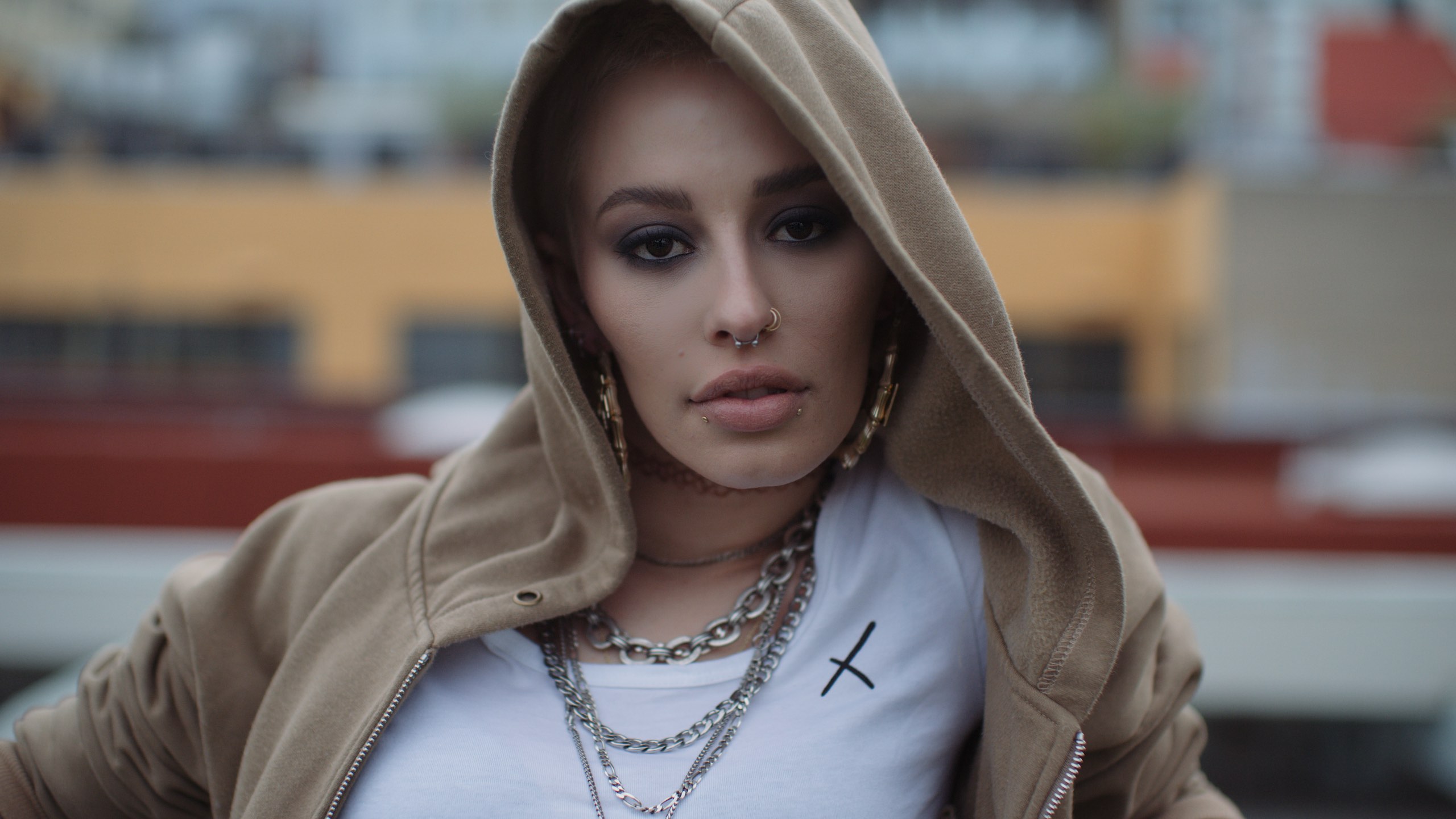 Headshot of woman with nose rings, earrings and chains wearing a beige hoodie