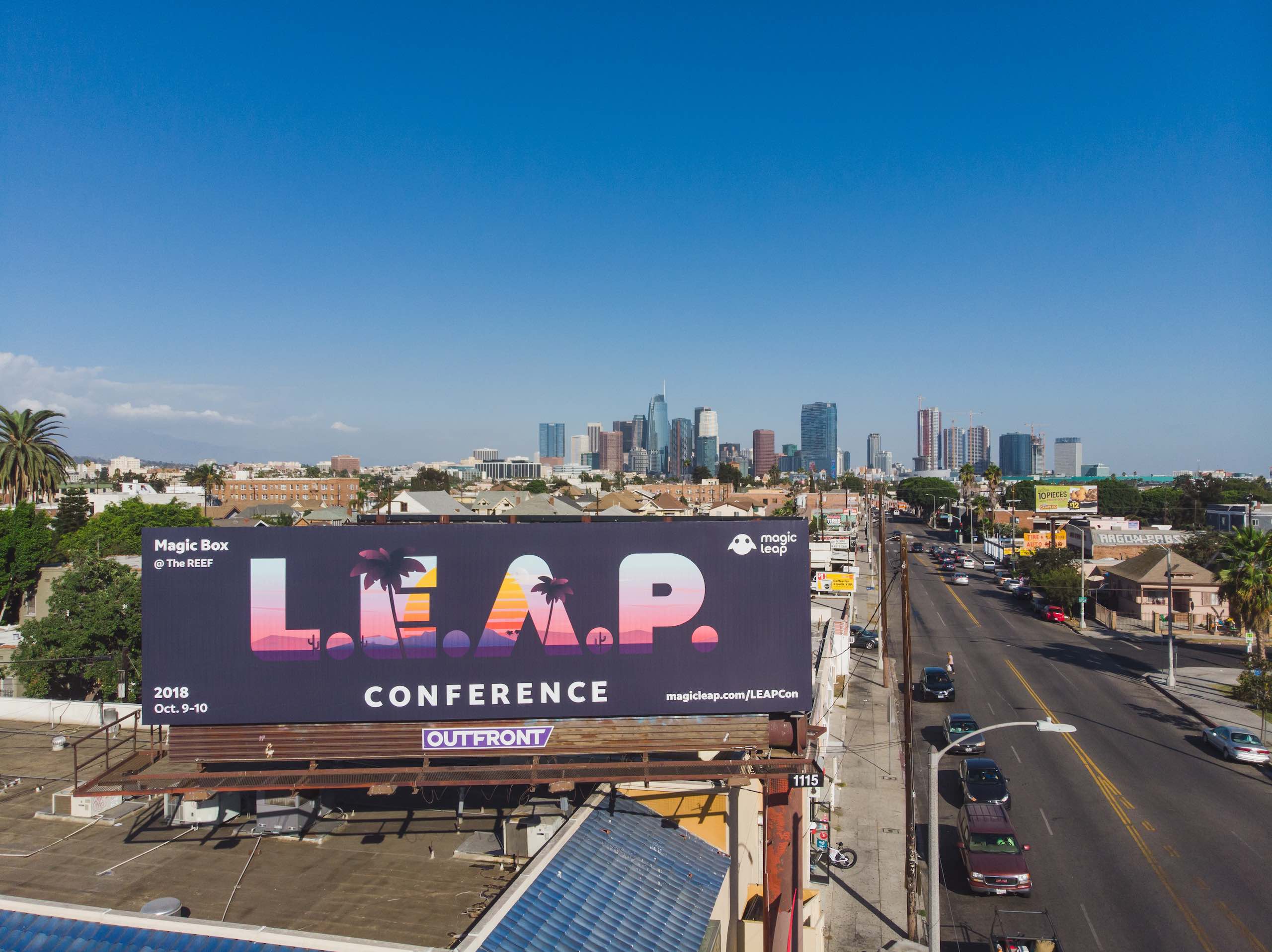 View from drone of LEAP Conference billboard on display near road with cars parked and driving by
