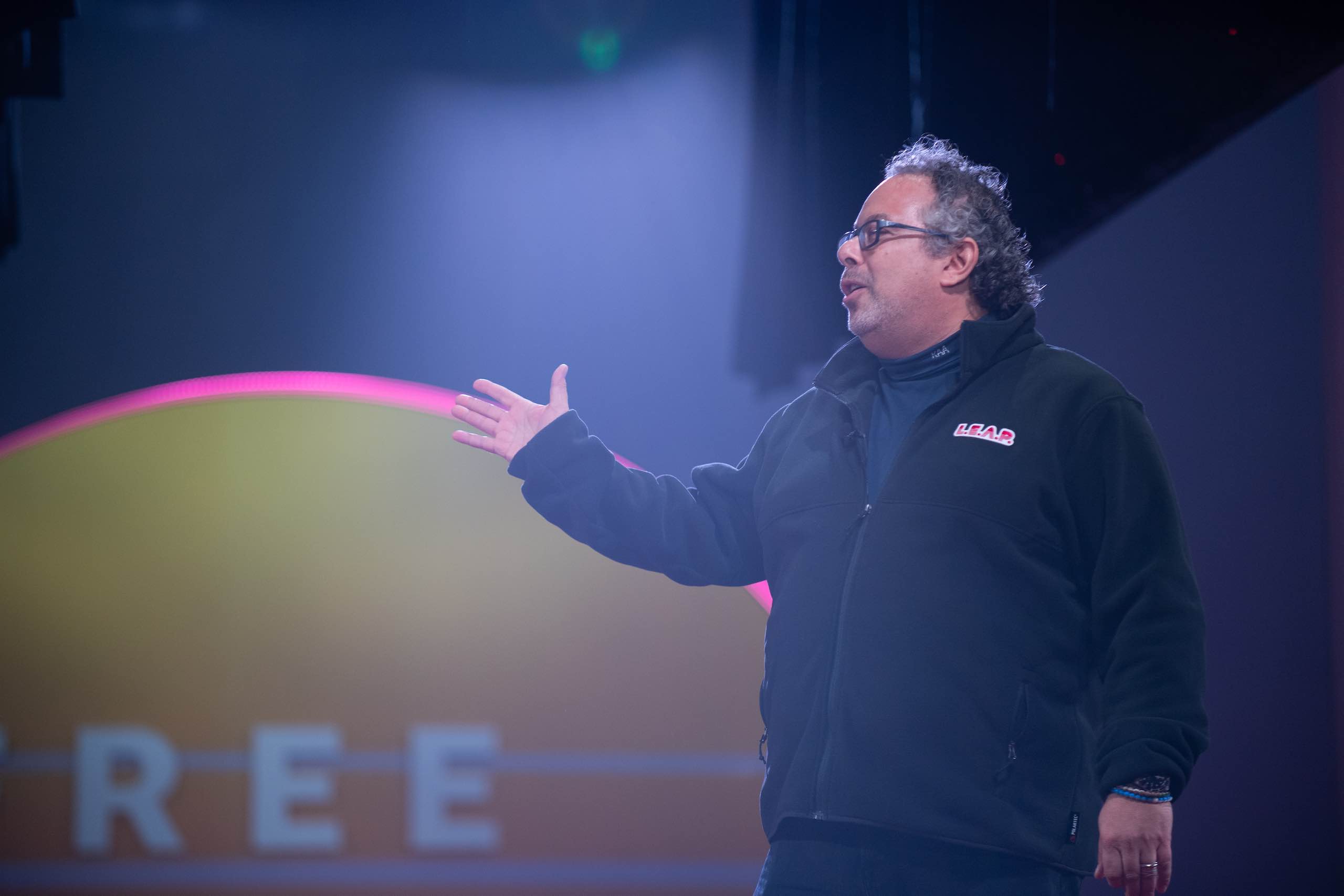 Side profile of man wearing glasses standing on stage at a Free Your Mind event