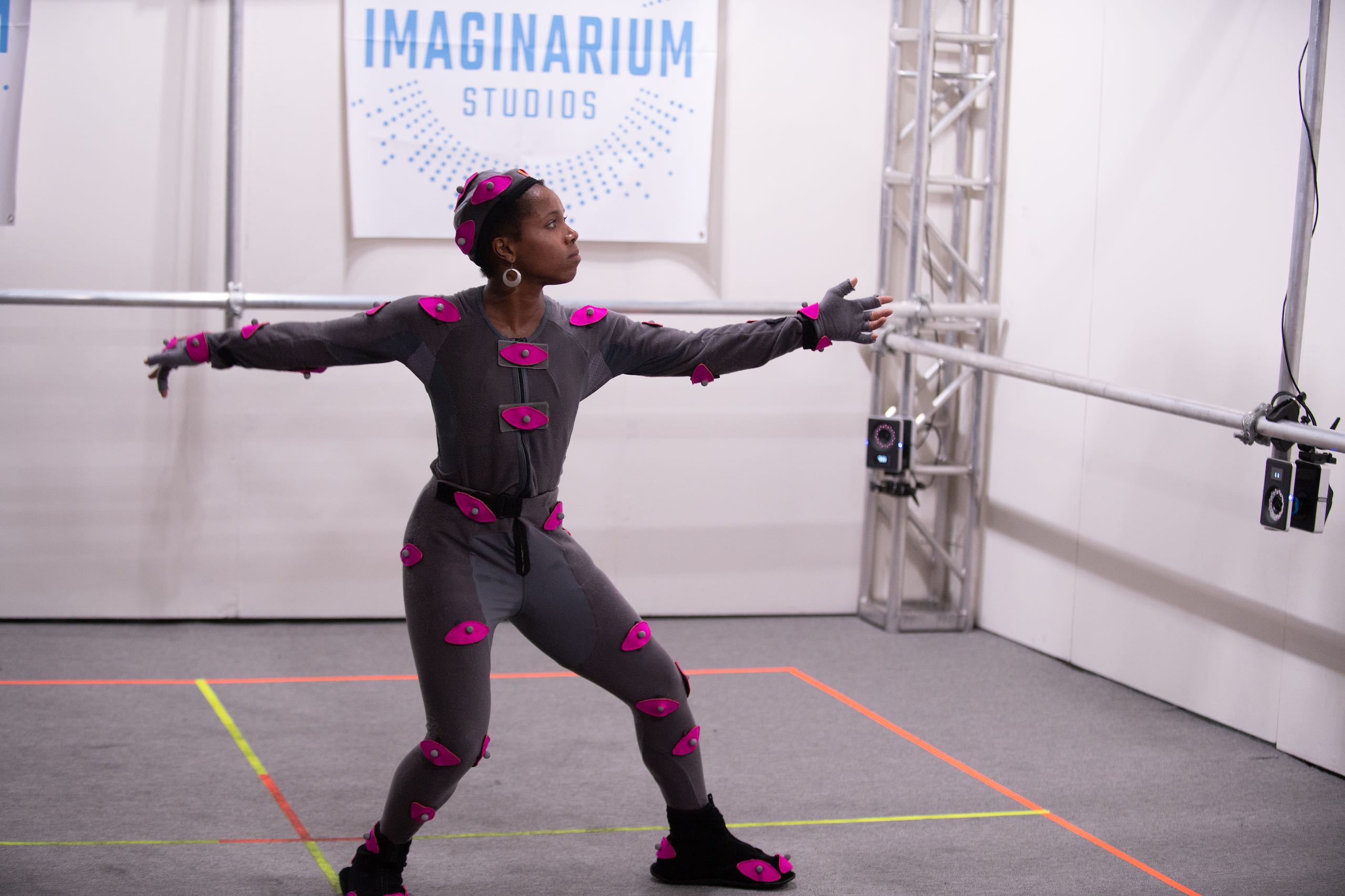 Woman with pink body movement sensors posing with arms outstretched in front of The Imaginarium Studios sign
