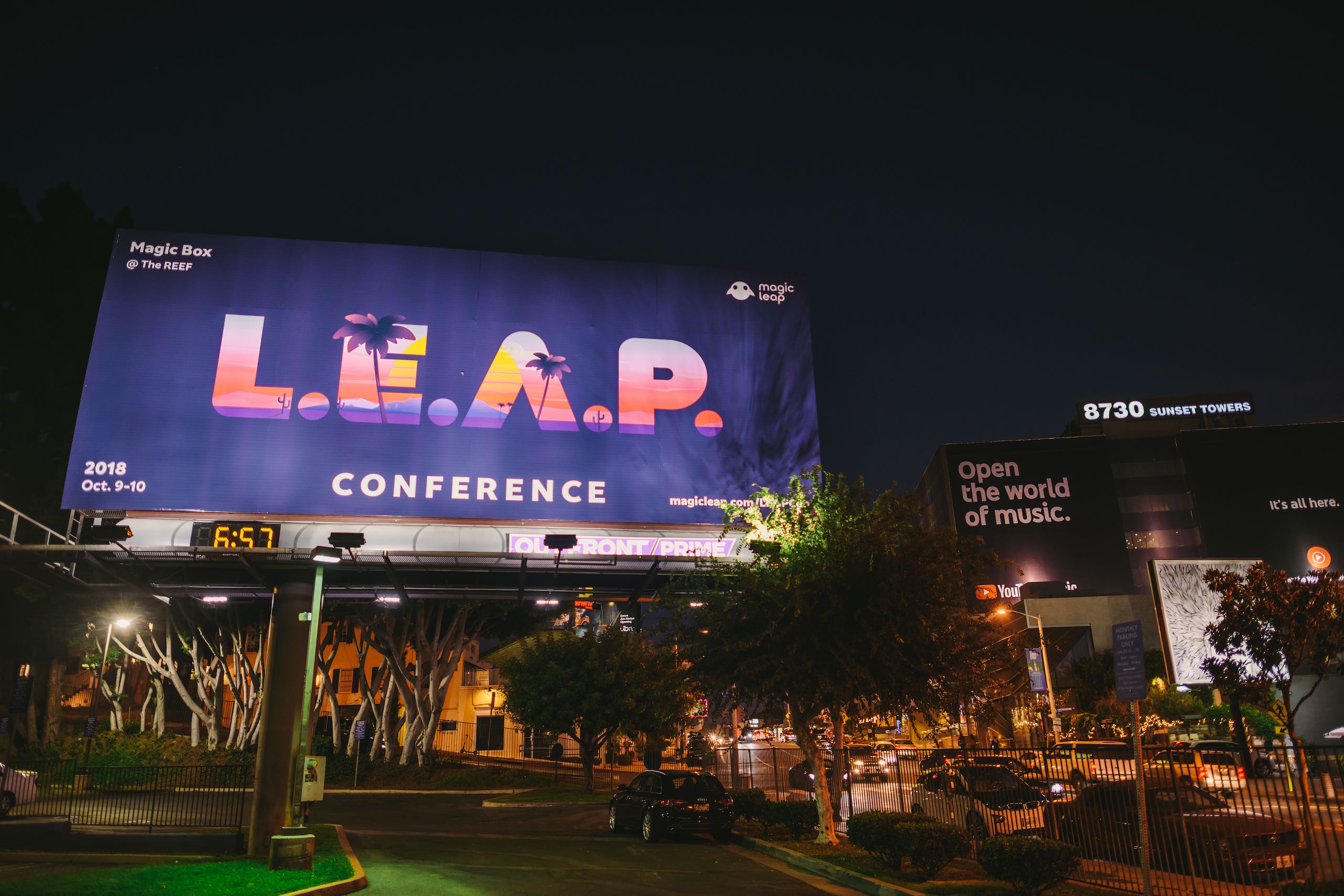LEAP Conference billboard on display by a parking lot in city near road with cars parked and driving by at night
