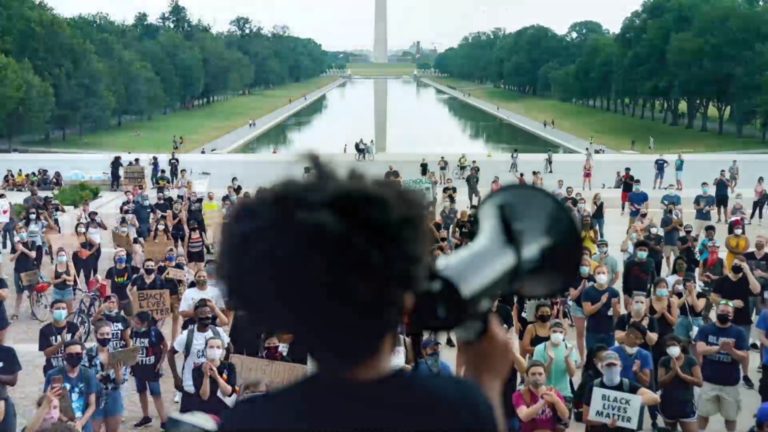 76 Words and Collective PAC, We Voting political ad View from behind of speaker with a bullhorn addressing a crowd on the Washington Mall