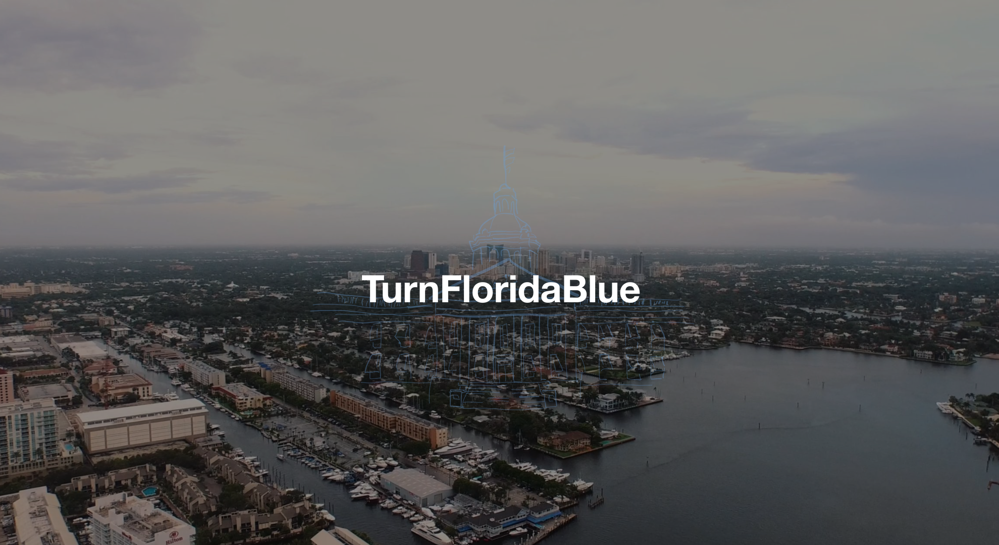 IU C&I Studios Page Florida House Victory Cindy Polo White Turn Florida Blue text on a backdrop aerial view of ports with boats