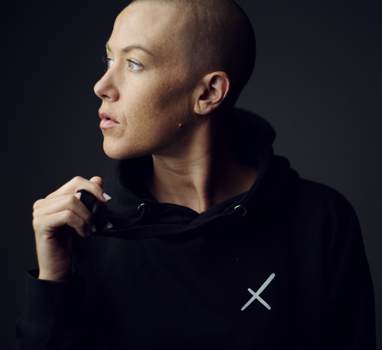 Uncreative Shop Headshot of female model with shaved head looking off to the side wearing black jacket with white Uncreative logo