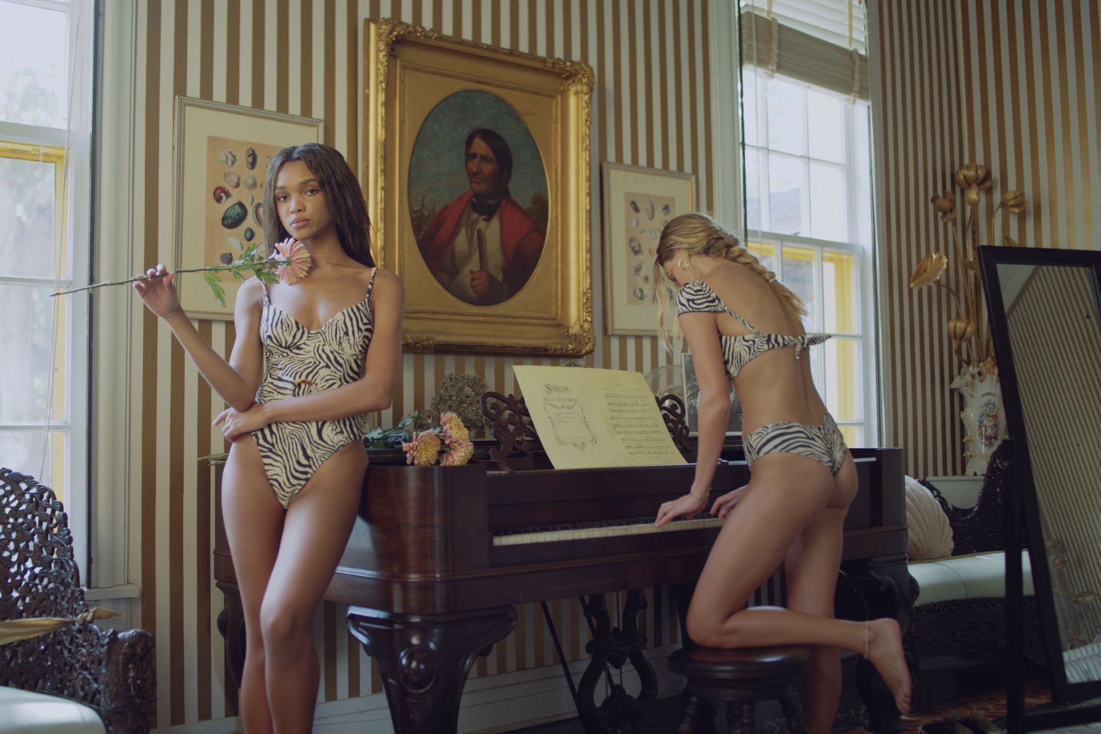 IU C&I Studios Page Production Resources Location with two women wearing black and white patterned swimsuits with one leaning against the piano holsing a flower and the other playing the piano