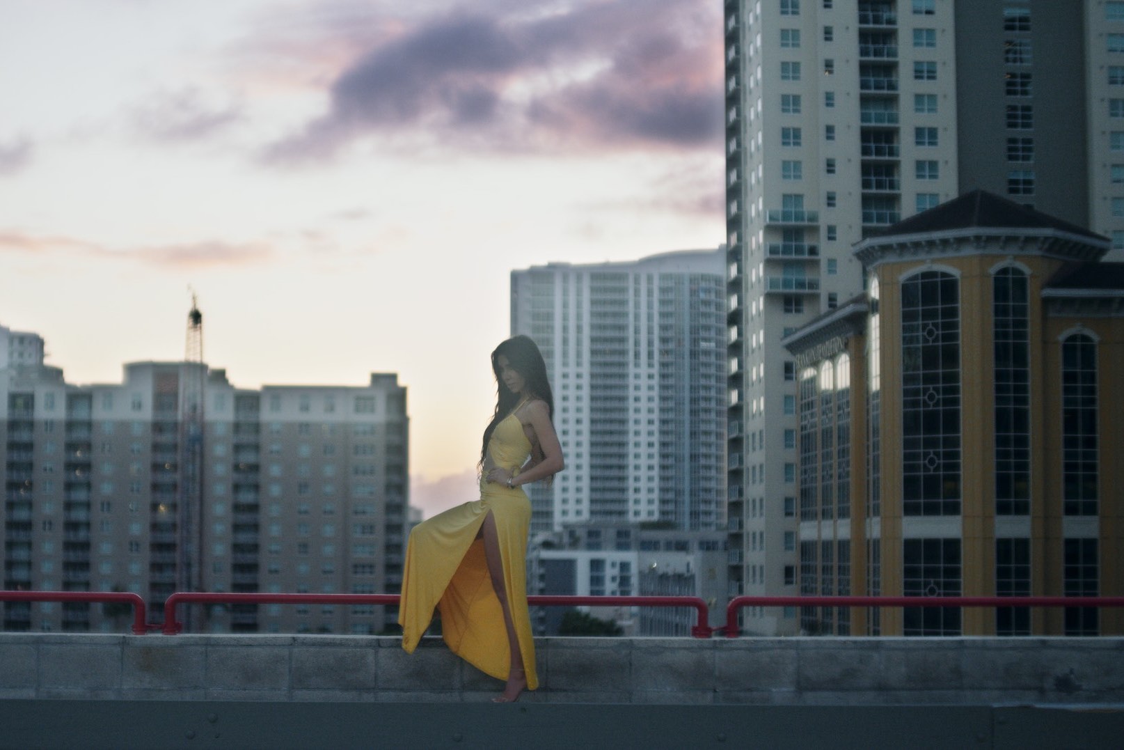 IU C&I Studios Page Production Resources South Florida Locations Side profile of woman wearing a yellow dress standing on a rooftop by a red railing in a city
