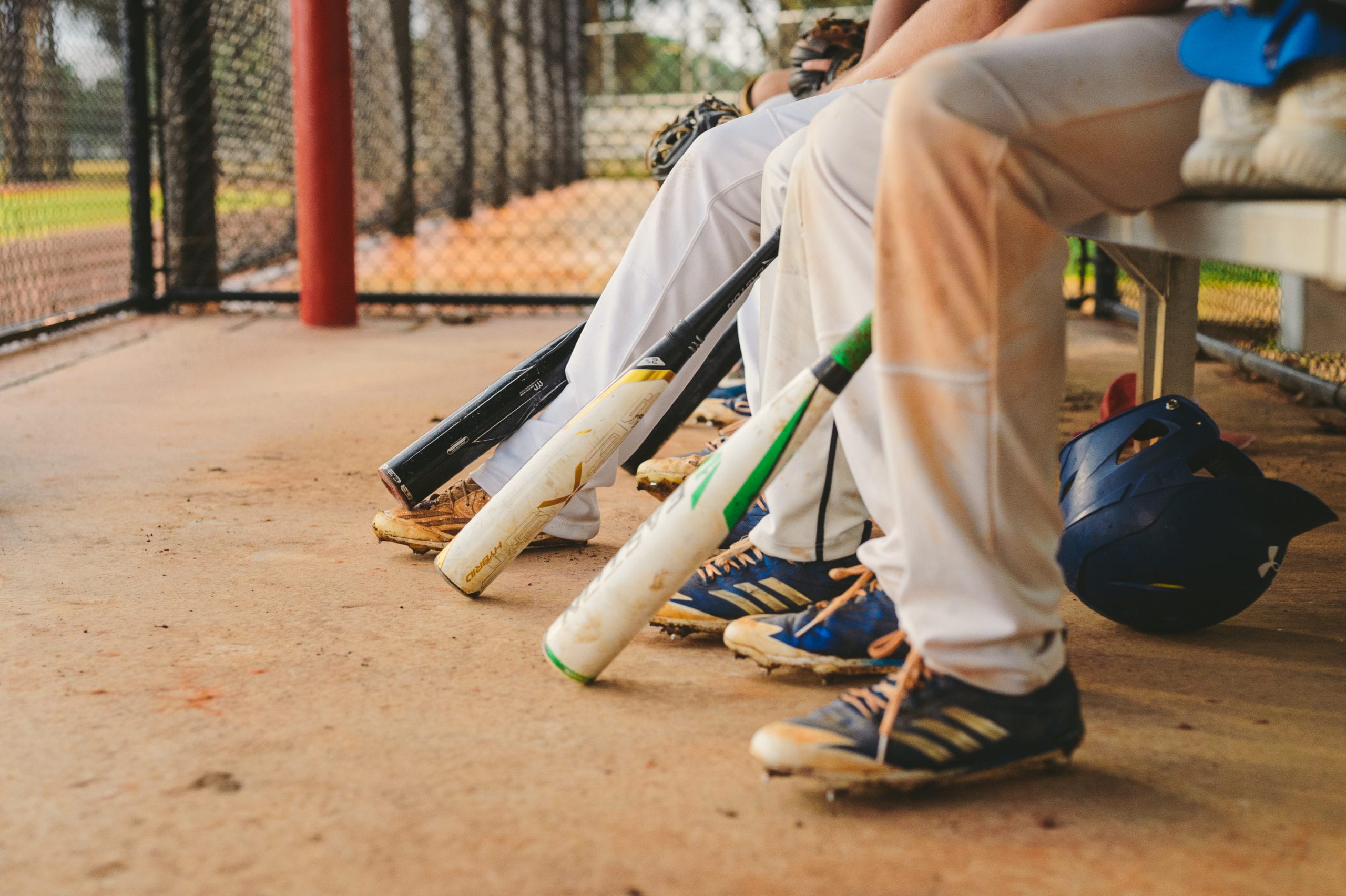 Closeup of lower halves of young baseball players wearing cleats holding bats while sitting on the bench