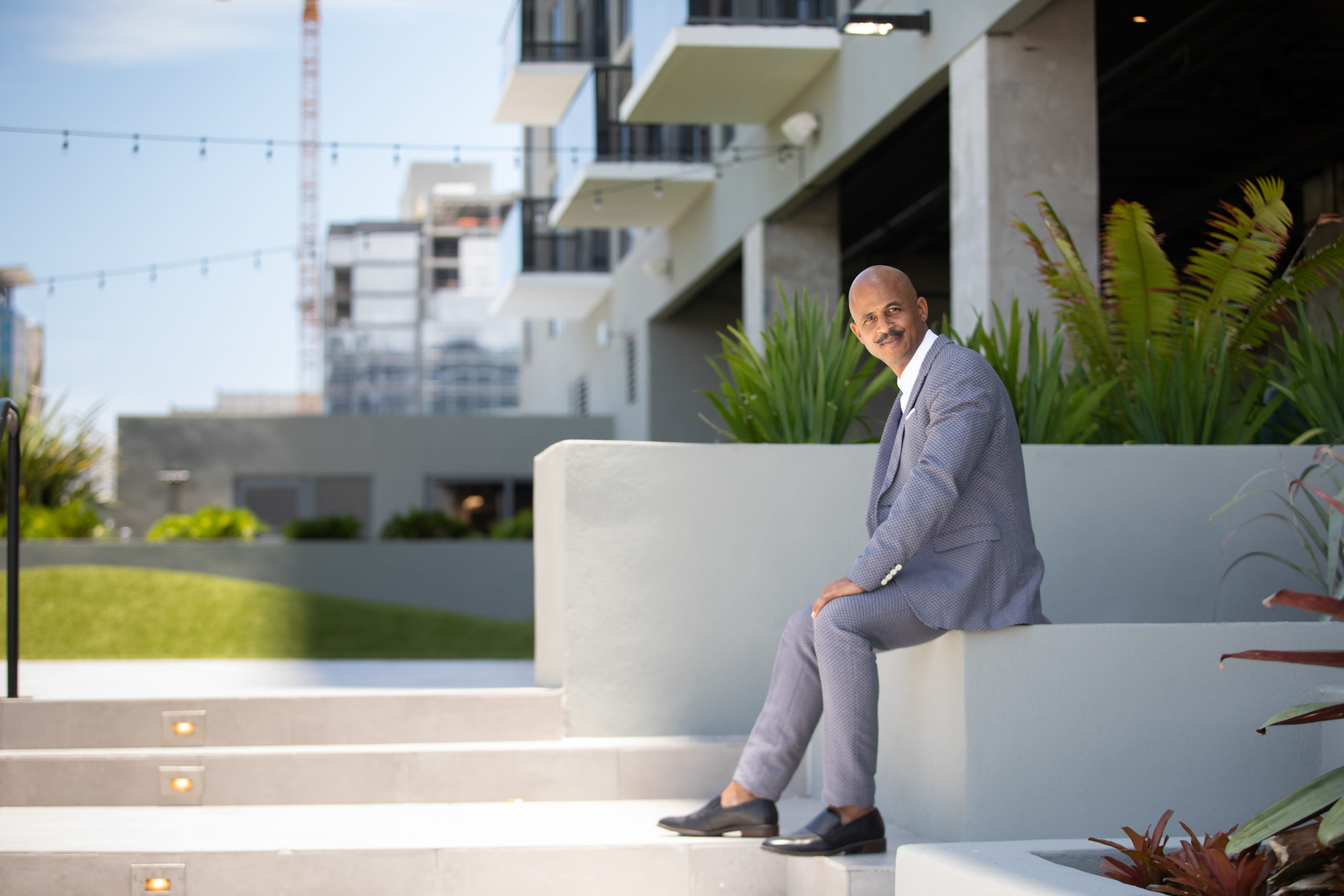 Fort Lauderdale Illustrated Men of Style Bald African American male model with moustache wearing gray suit and white shirt sitting near stairs