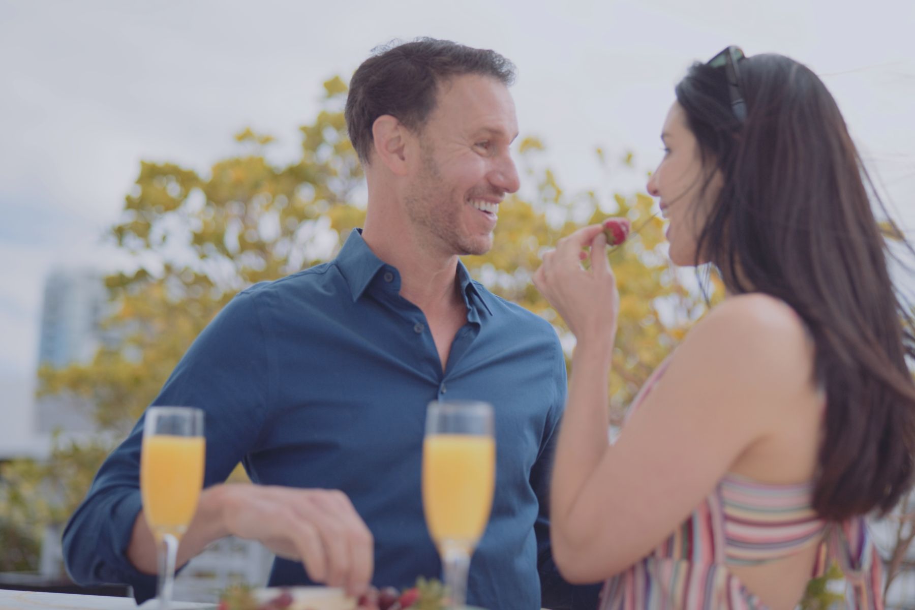 Macken Koya Bay Man and woman looking at each other by a plate of fruit and drinks while woman eats a strawberry