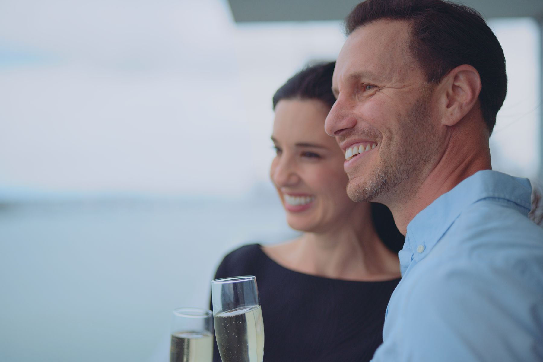 Macken Koya Bay Side profile of man and woman smiling looking out over the water holding drinks
