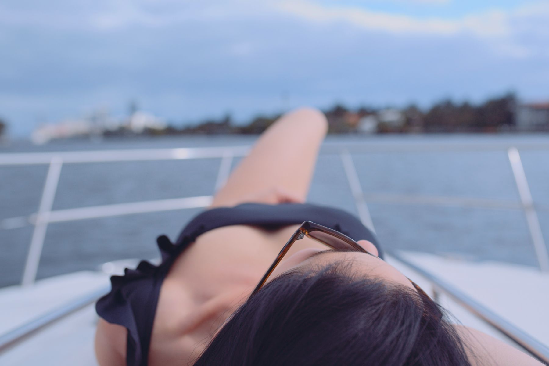 Macken Koya Bay Closeup of a woman wearing a black bathing suit and sunglasses sunbathing on a white yacht