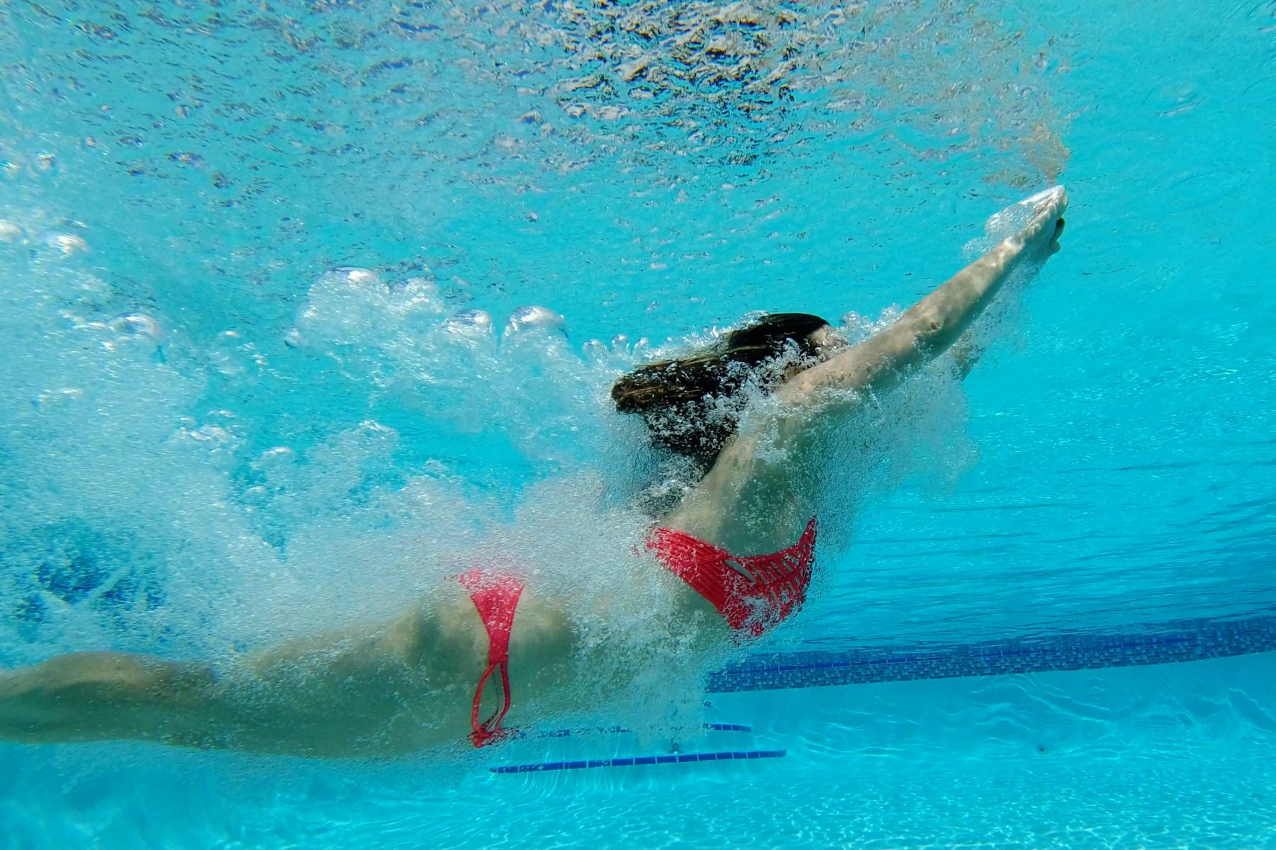 Macken Koya Bay Underwater view of woman wearing a red bikini swimming through the water in a swimming pool