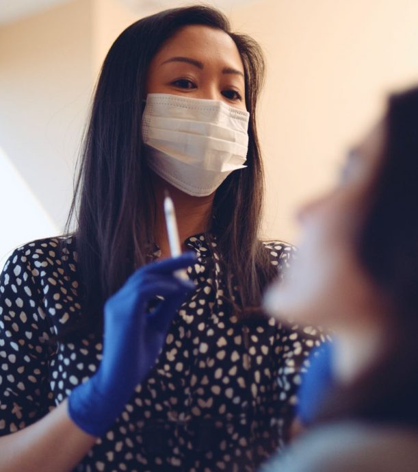Female dental assistant wearing a white mask looking at patient
