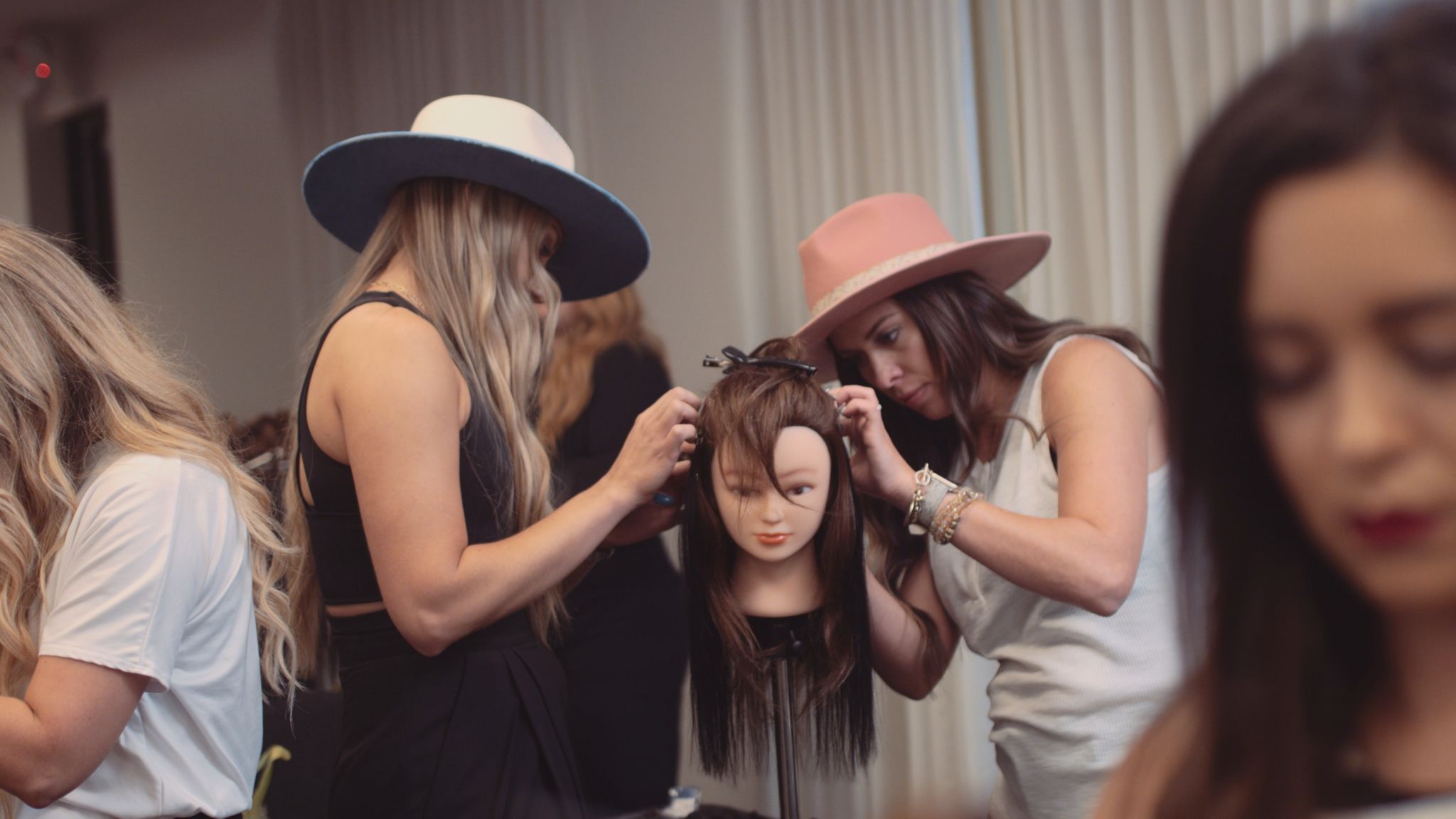 Aqua Hair Extensions Stills Two women wearing hats working on a wig on a female dummy