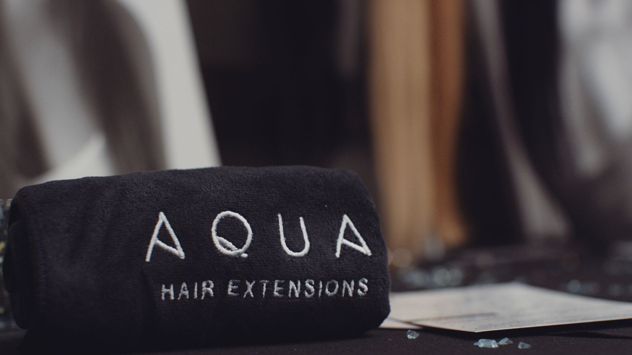 Aqua Hair Extensions Still Closeup of black towel with white logo