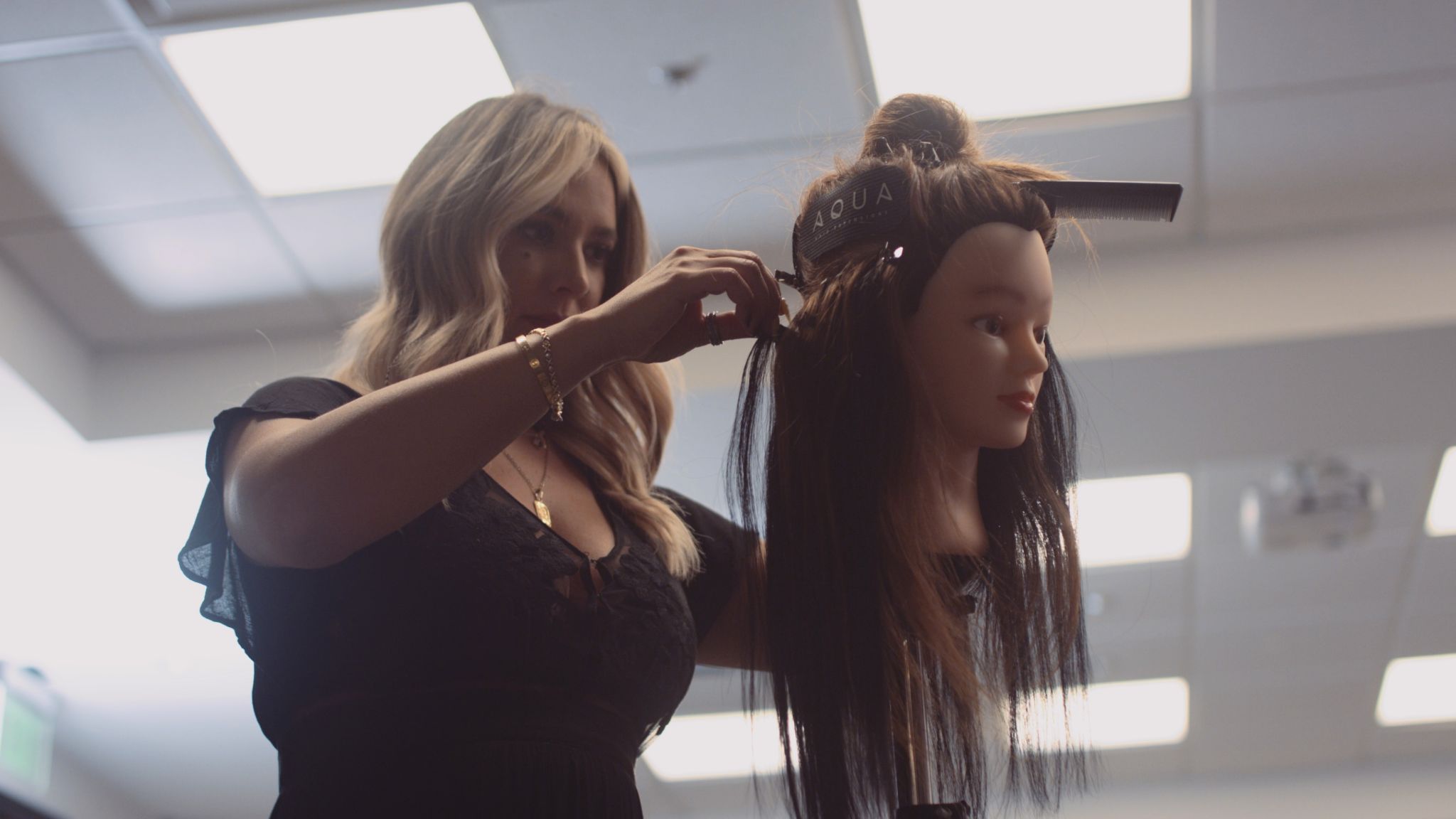 Aqua Hair Extensions Still Side view of woman with long blond hair working on a female dummy model with a wig