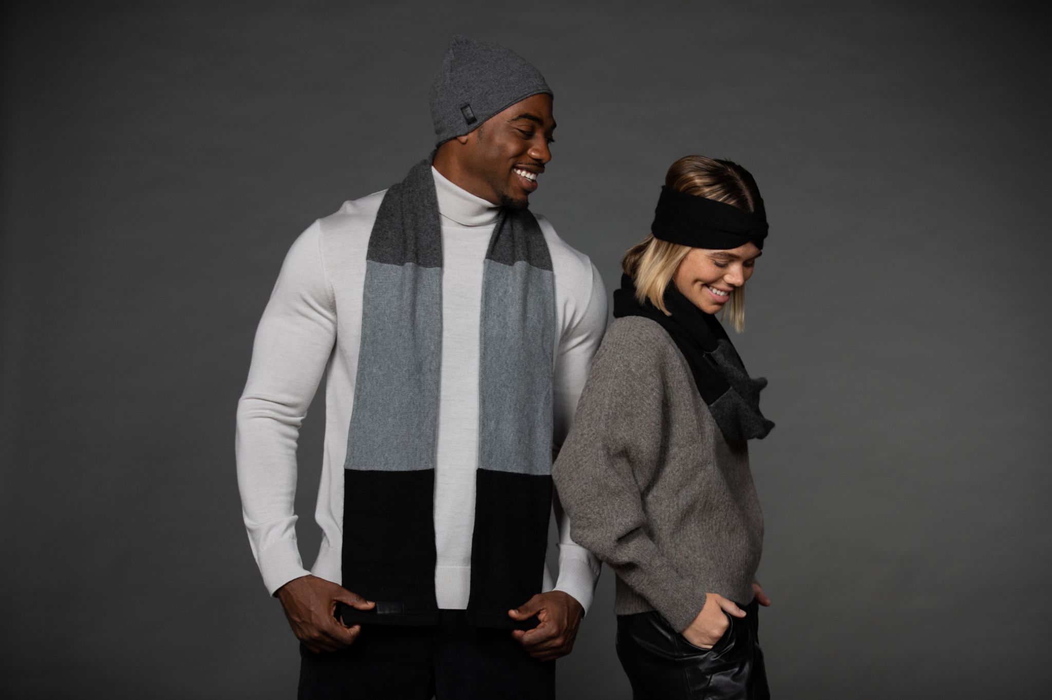African American male model looking over to the side profile of a female model looking down posing for the camera smiling against a gray backdrop
