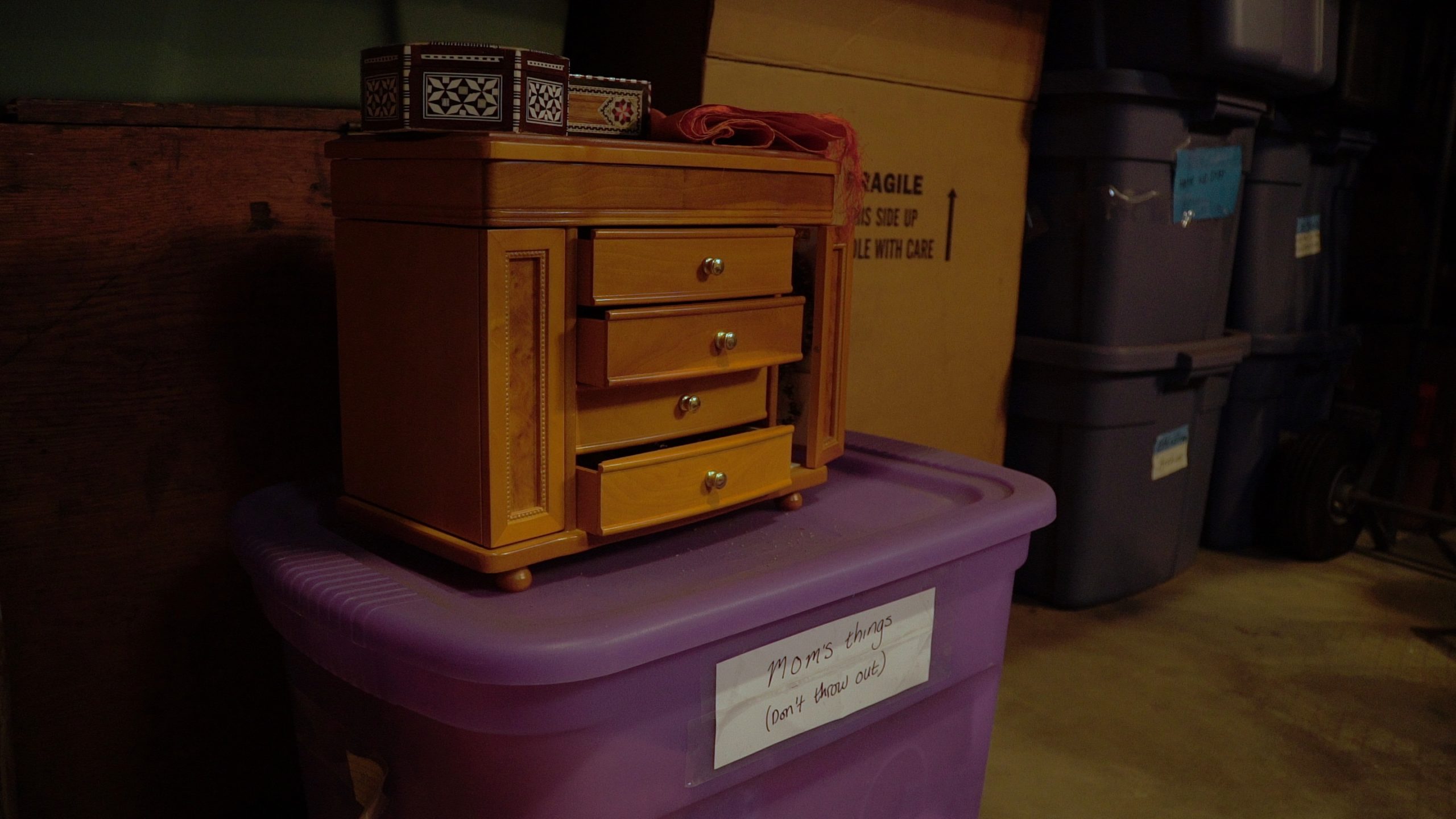 Closeup of small table with drawers sitting on a purple tote in a storage room with other totes and boxes