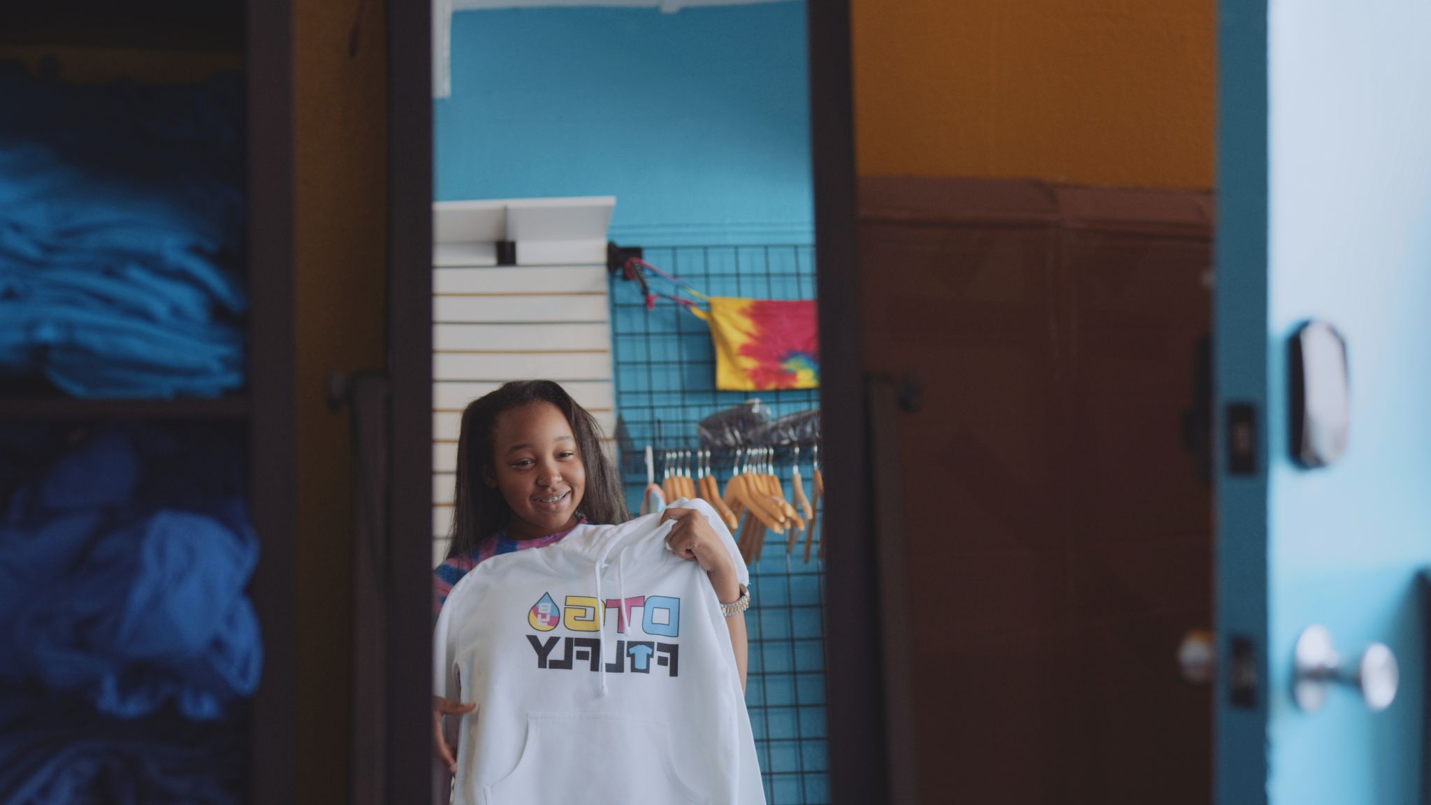 Girl holding a white sweatshirt with logo looking in a mirror smiling