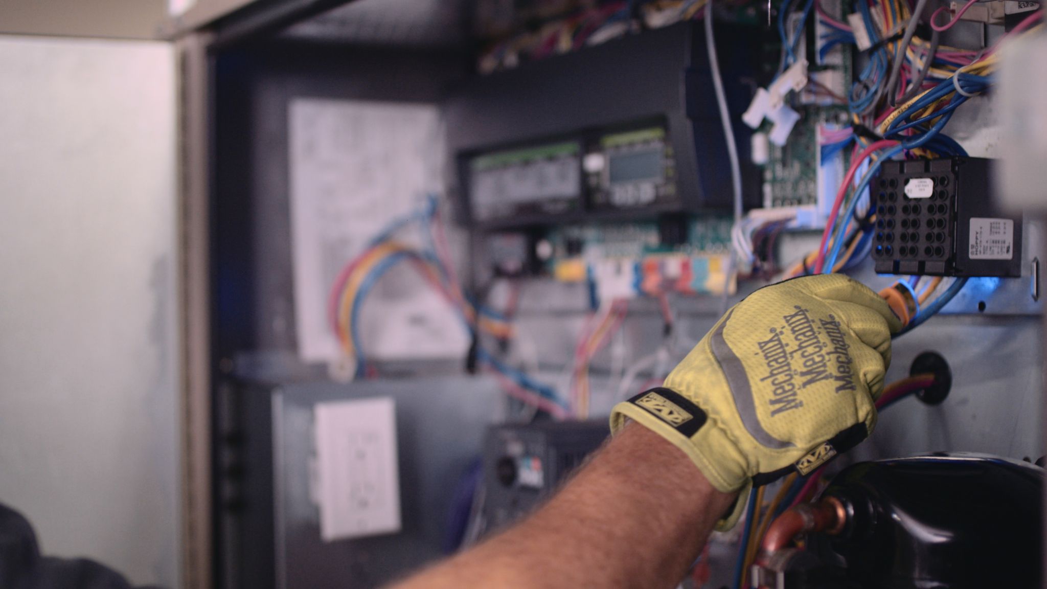 Closeup side profile of a man wearing a yellow glove working with electronics in a container