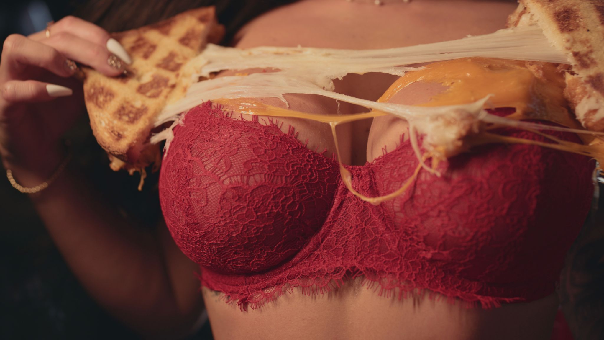 Closeup of grilled cheese sandwich being spread across a woman wearing a red lacy bra's chest