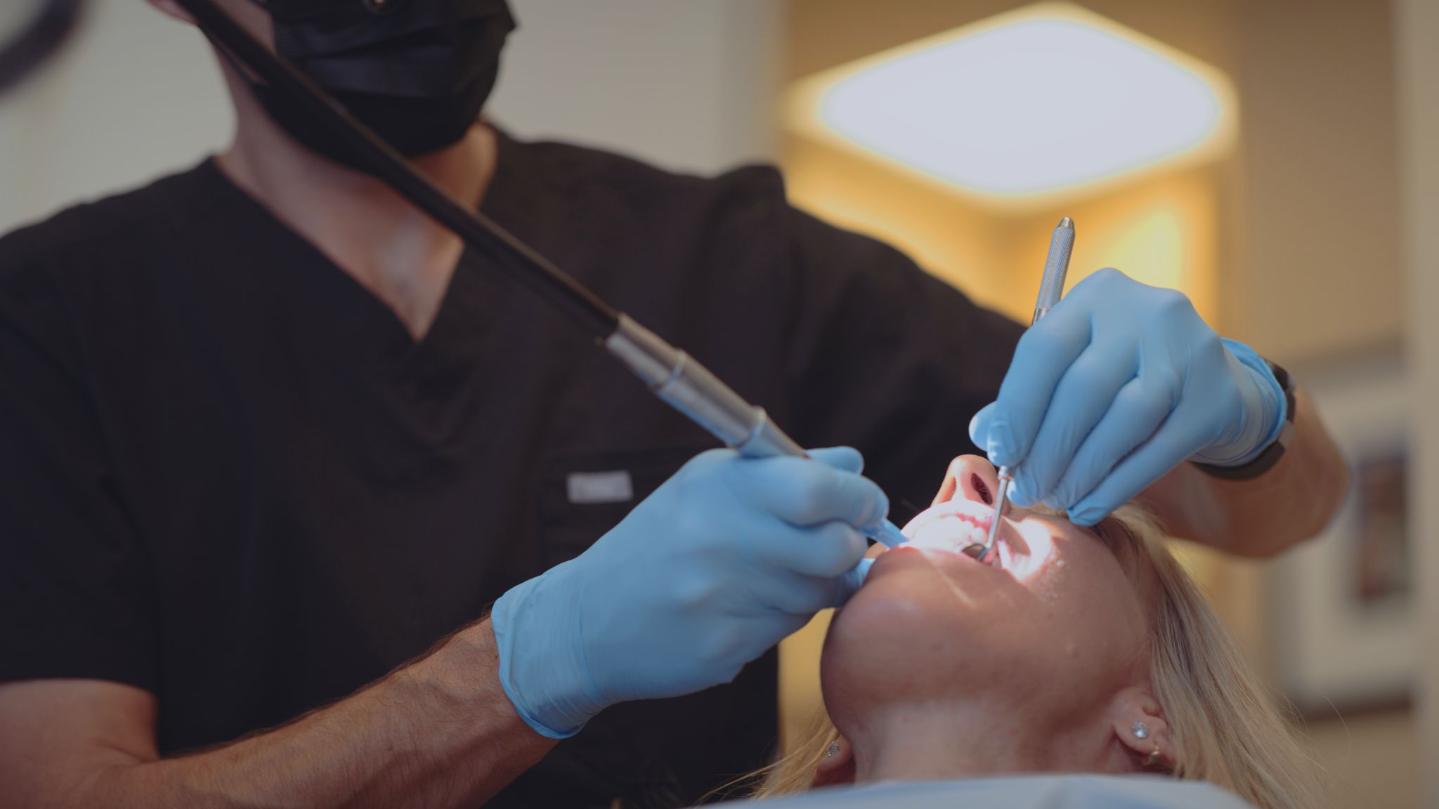 Male dentist wearing black mask working on a female patient
