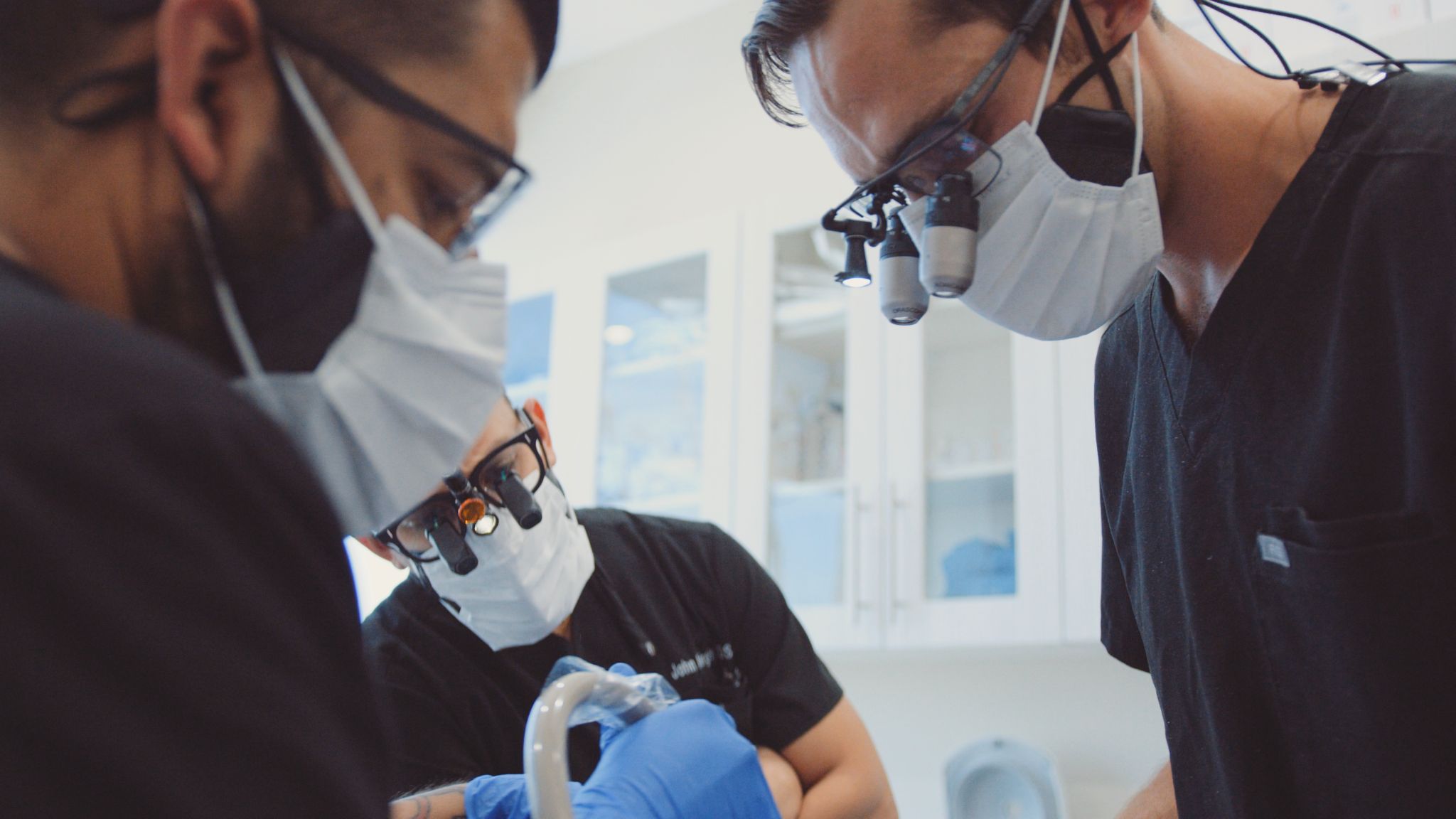 Two male dentists and a male assistant working on patient
