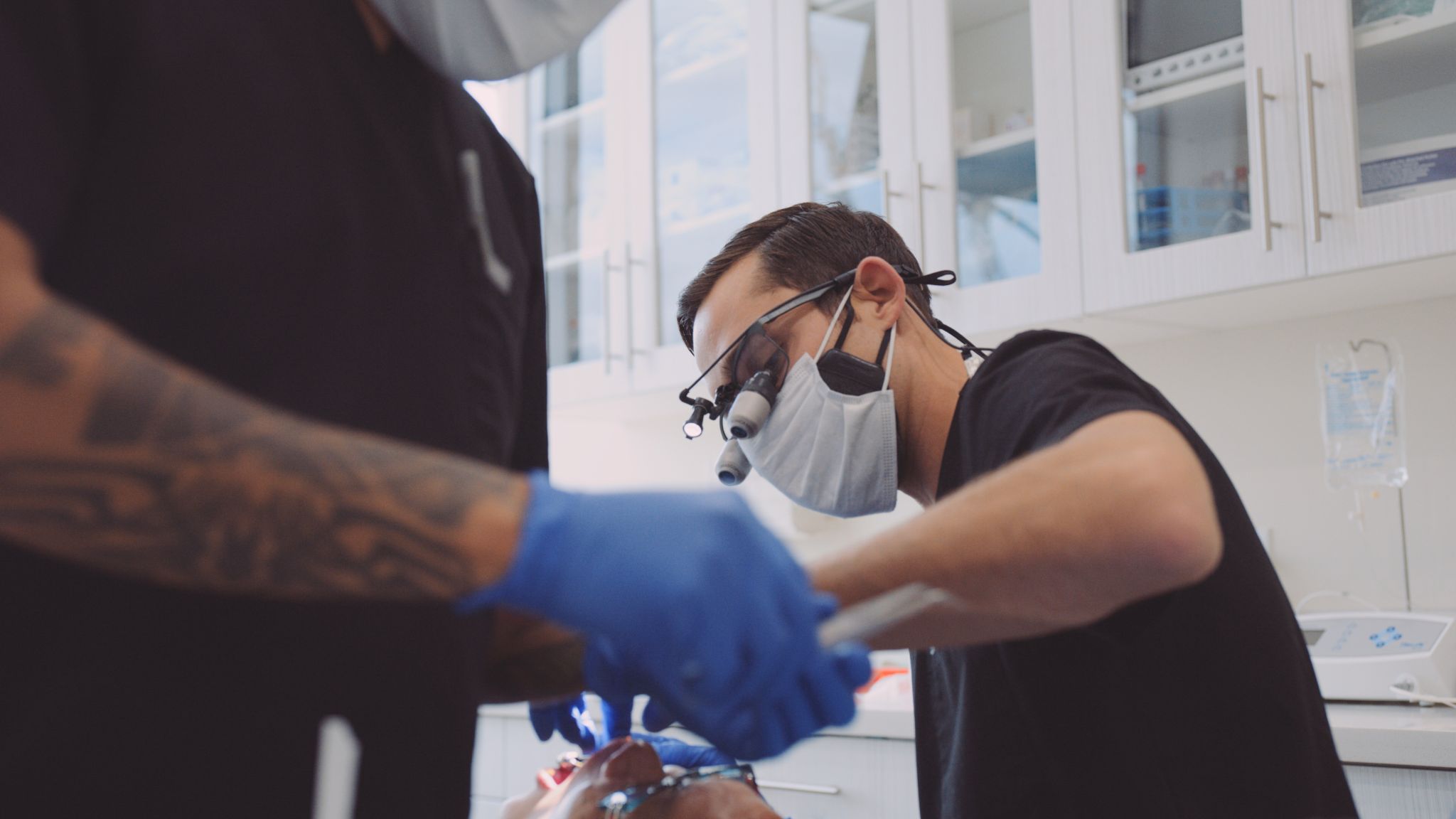 Male dentist working on teeth while male assistant gets equipment