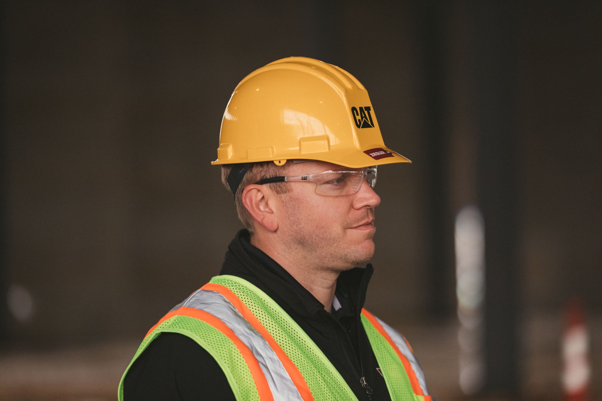 Side profile of a worker wearing a hard hat, glasses and safety vest