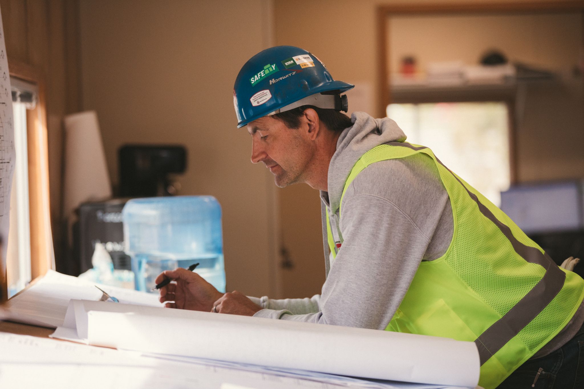Side profile of construction worker wearing a blue hardhat and safety vest looking over a blueprint