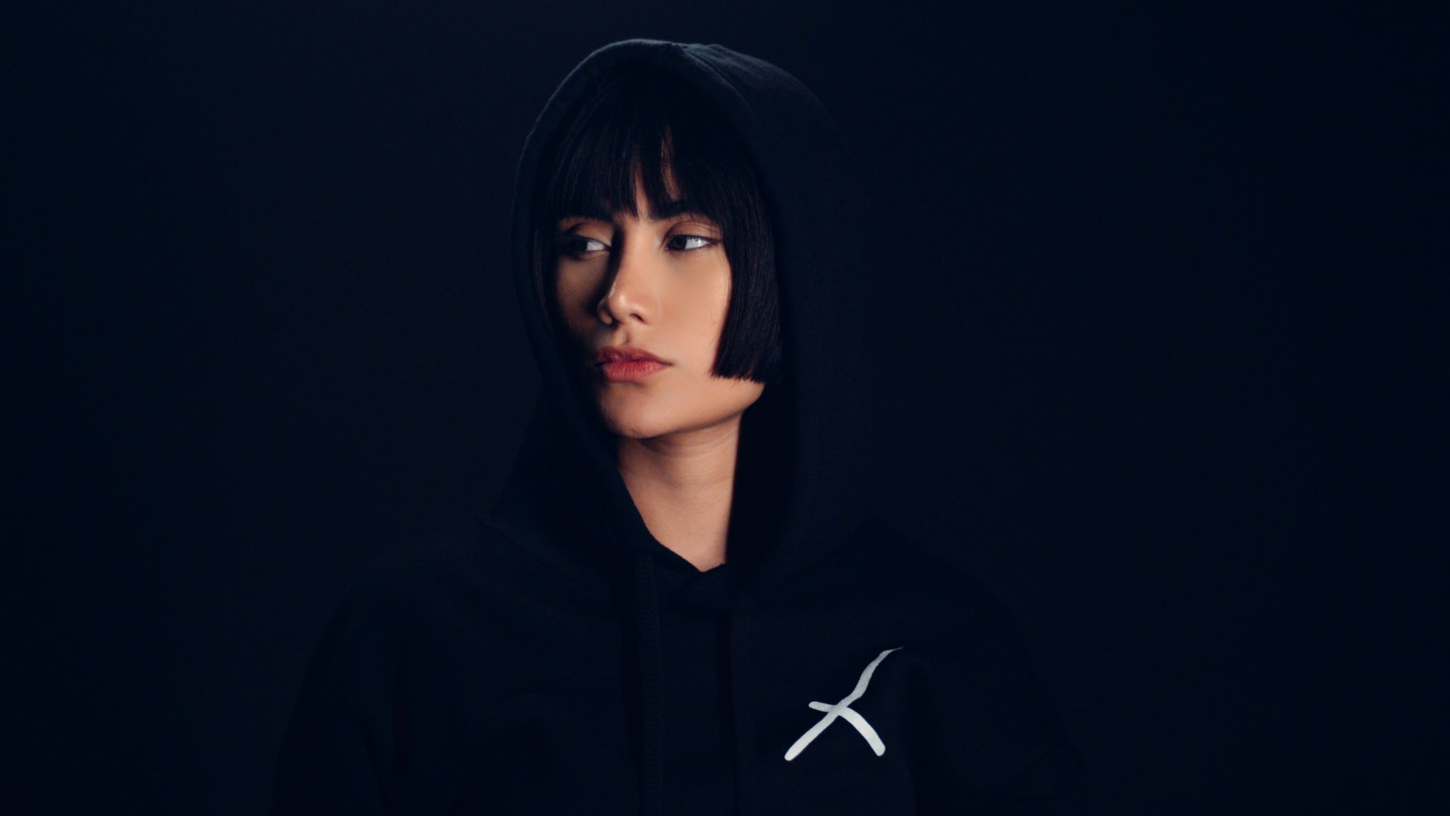 Female Model with short hair posing for the camera in darkness looking off to the side wearing a black sweatshirt with white Uncreative logo
