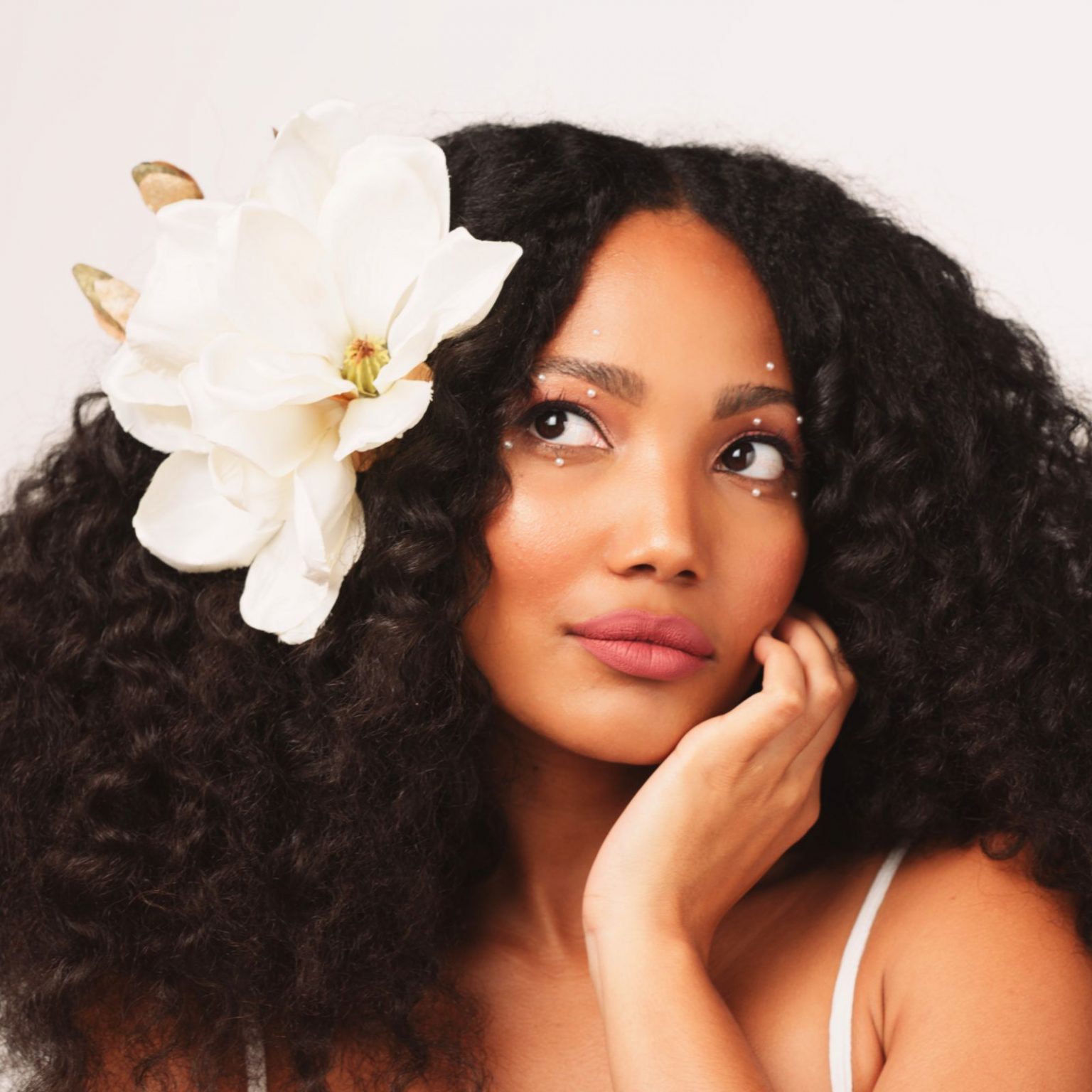 Woman With Black Curly Hair With A White Flower In It Posing For The Camera