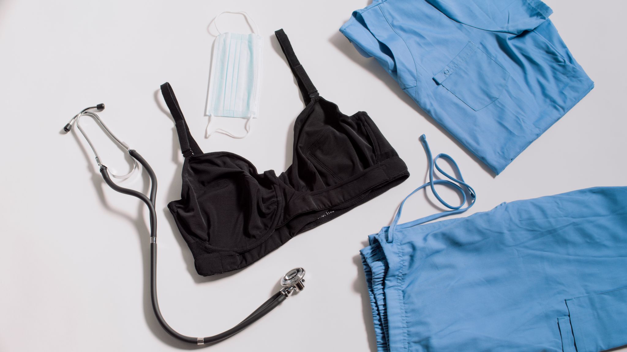 JENNAbra Product Flatlays Black bra on display with stethoscope, mask and light blue scrubs