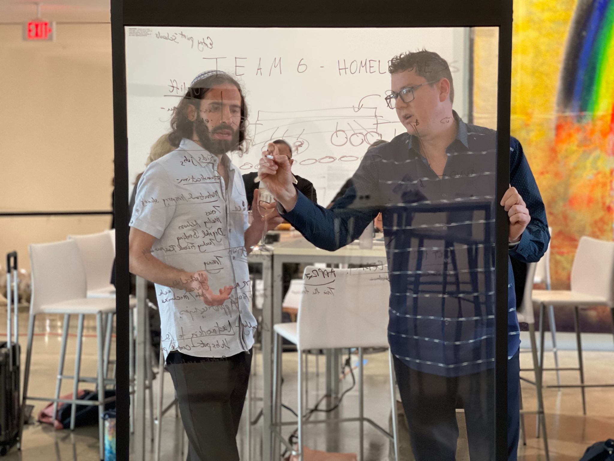 Why your Q1 Marketing Plan Should Include Video Content Man writing on clear board with marker while another man holding a glass of wine looks on