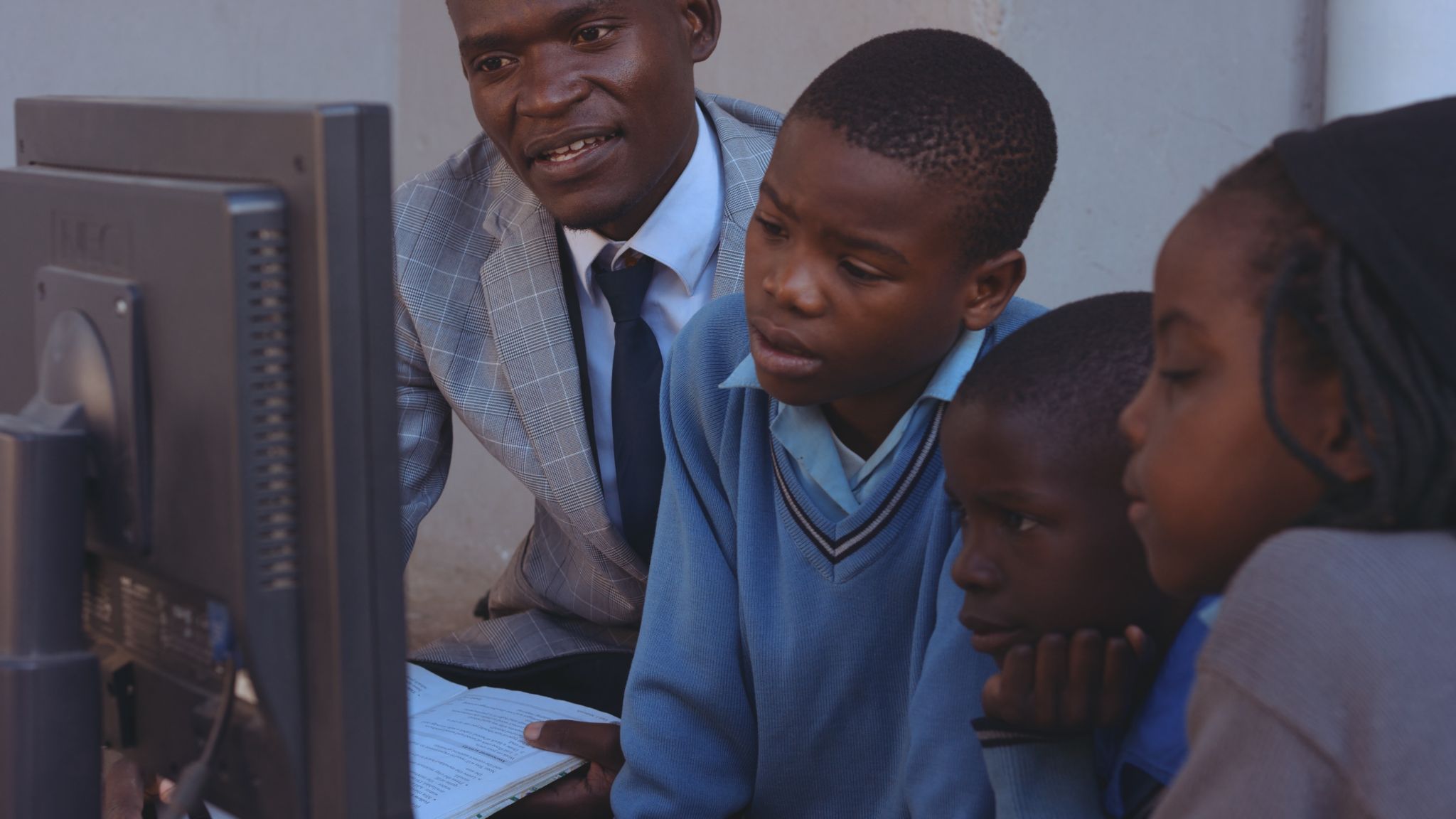 African American male teacher showing two African American boys and a girl something on a computer