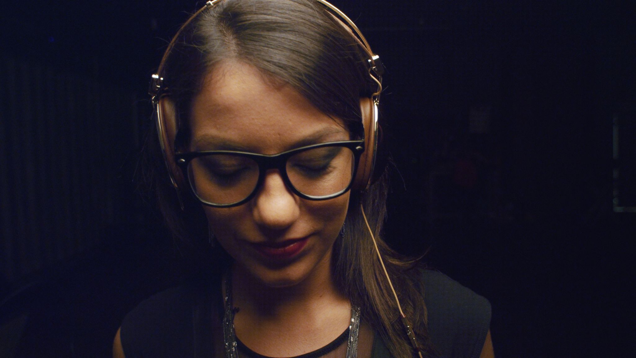 Woman wearing brown headphones and glasses looking down