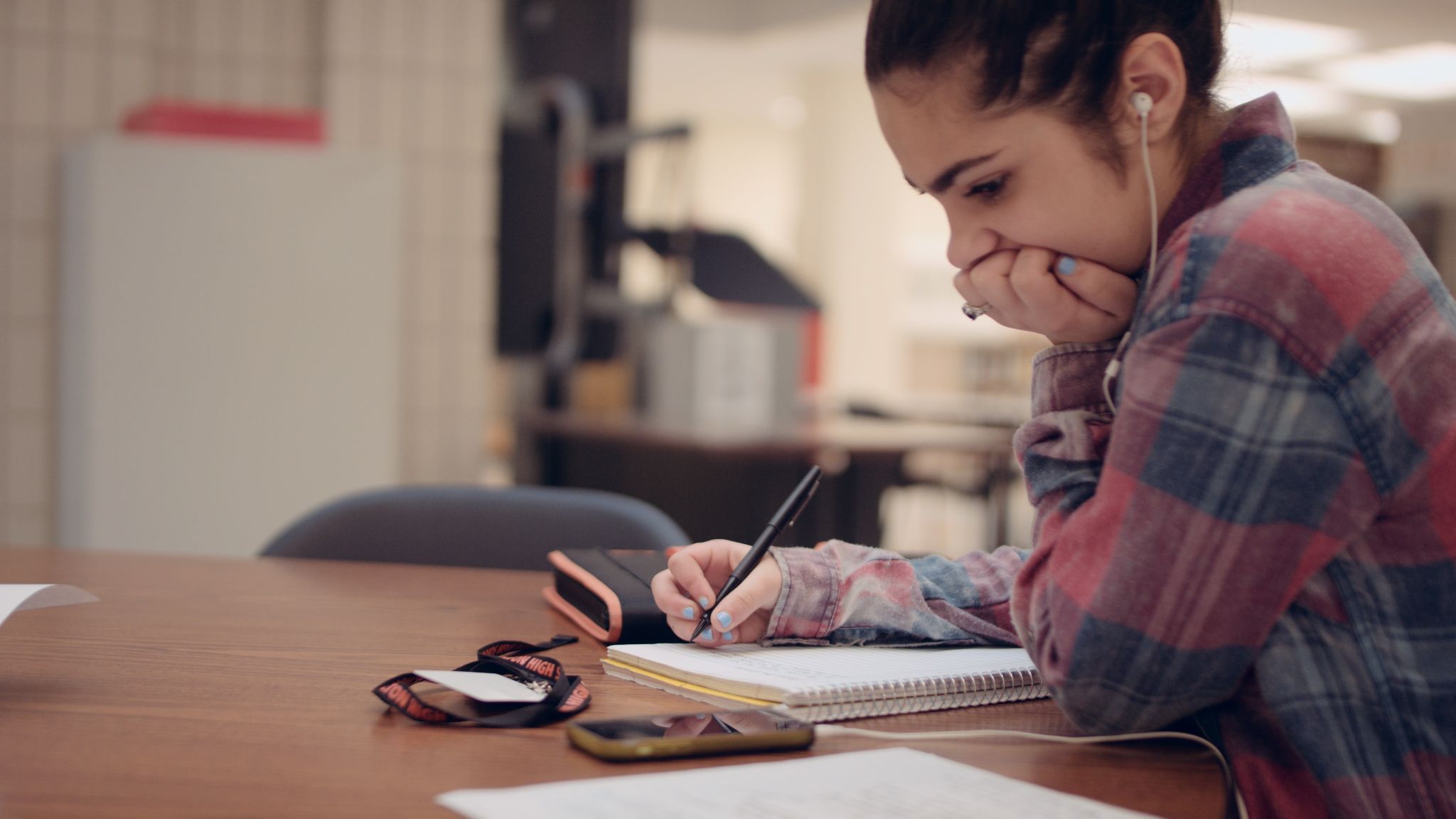 Side profile of girl doing homework at a table wearing white earbuds