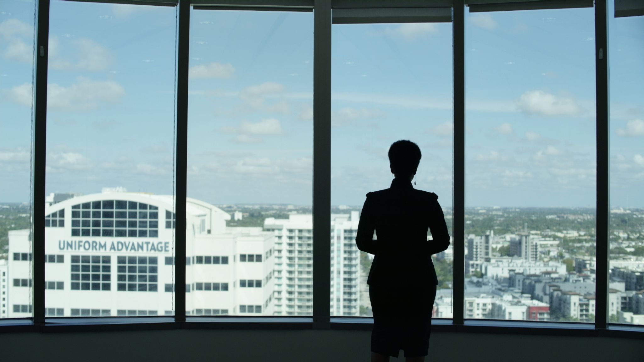 View from behind of woman looking out window over the city in an office