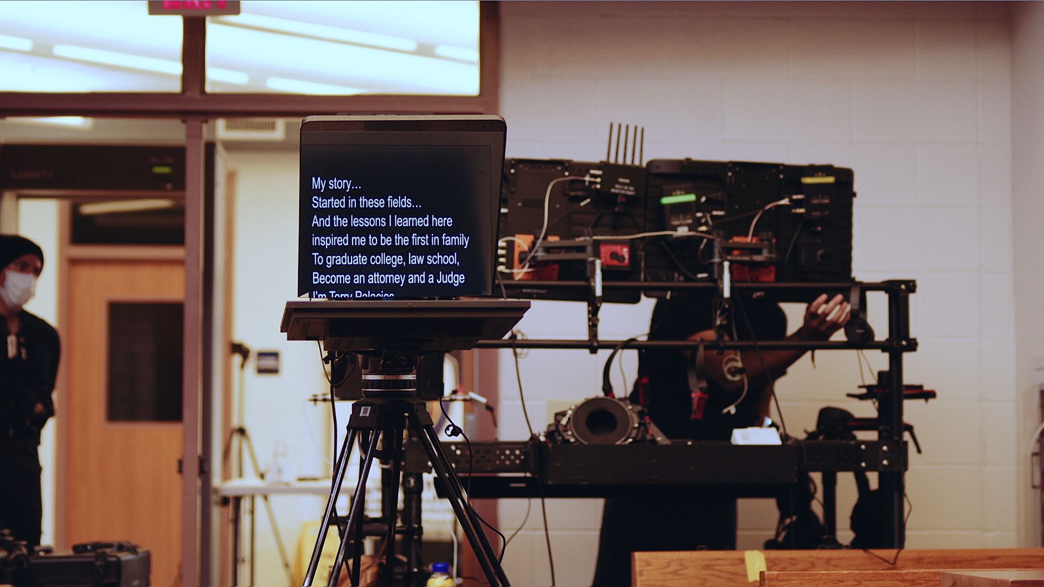 Closeup of teleprompter with two staff members nearby